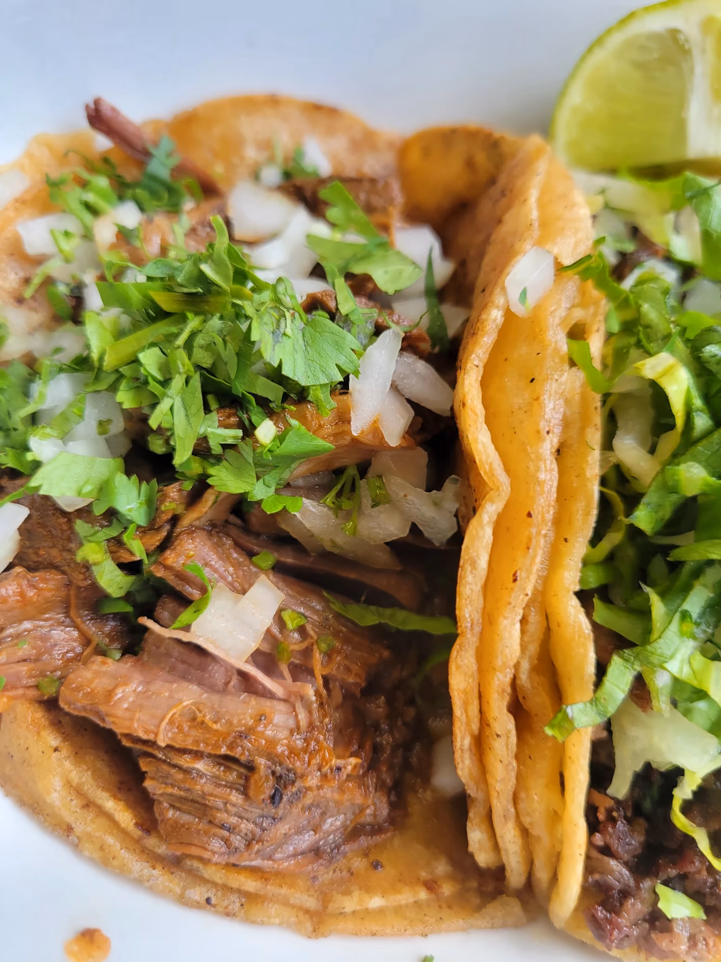 Close-up of a shredded barbacoa taco with onion, cilantro, and lime at Don Chuy's Taqueria