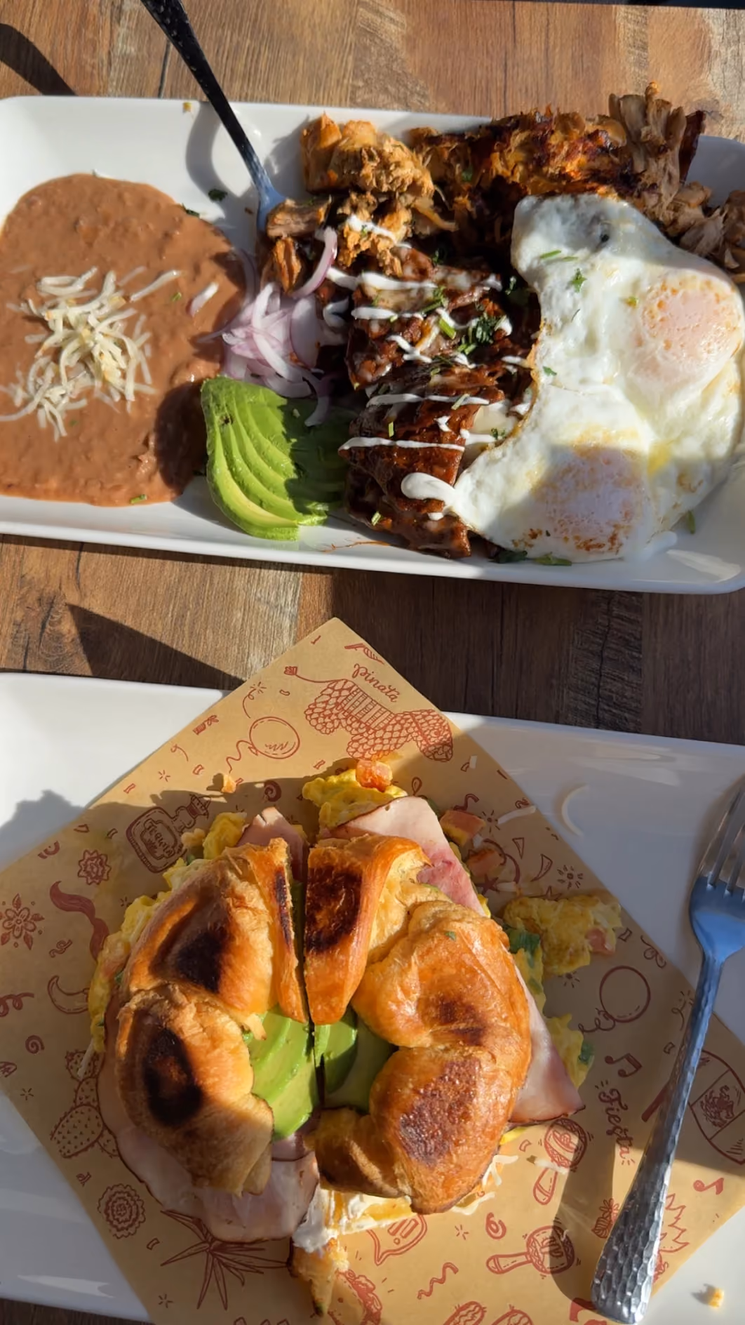 Breakfast plate with pulled pork, fried eggs, and avocado alongside a ham and avocado croissant breakfast sandwich at Don Chuy's Taqueria