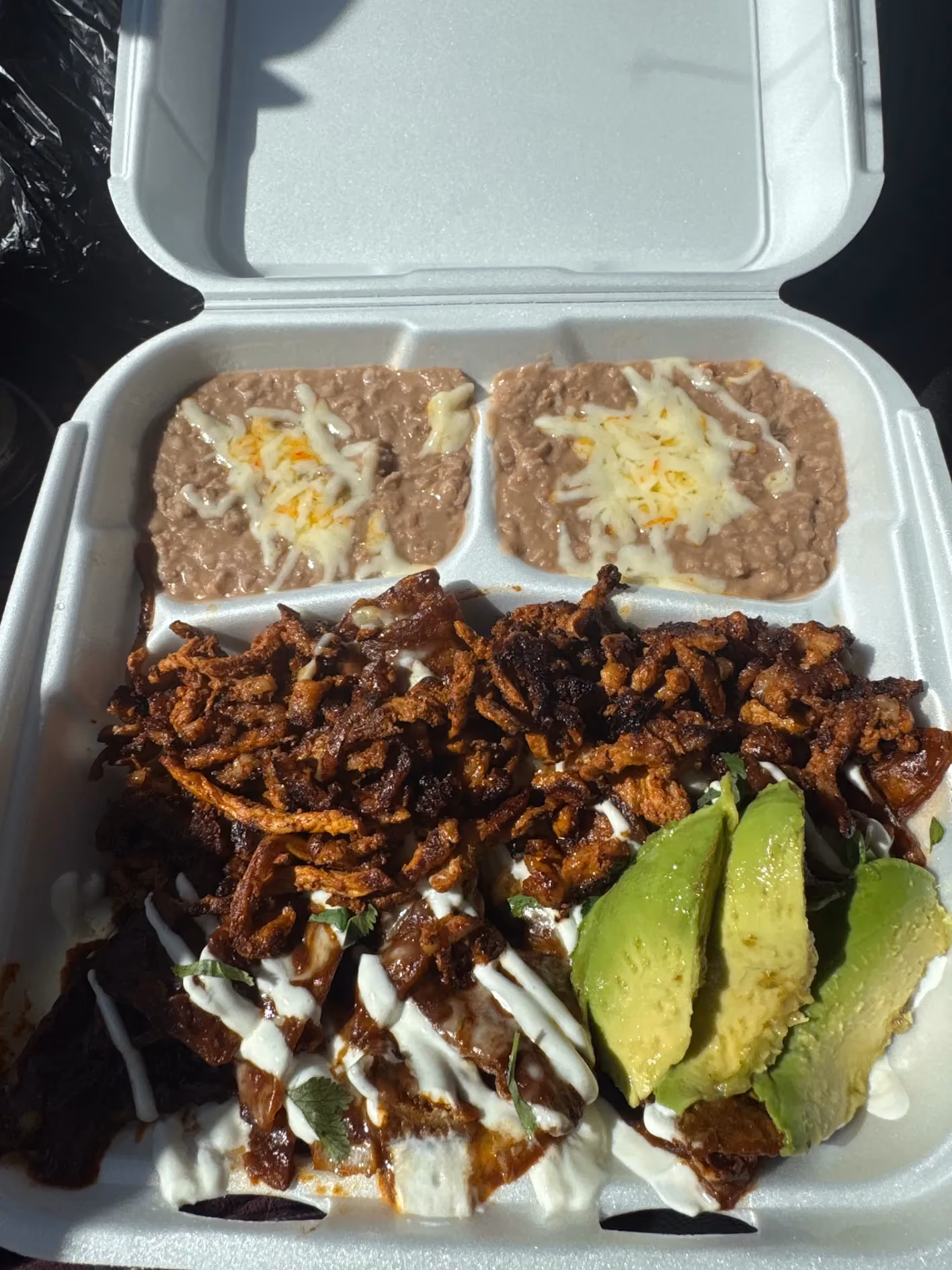 Crispy tacos with sour cream, avocado, and refried beans in a to-go container at Don Chuy's Taqueria