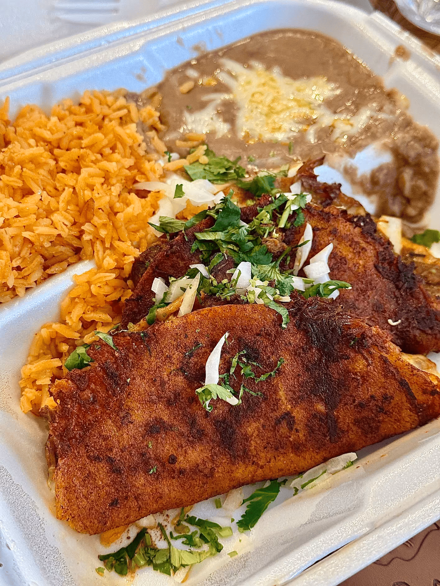 Crispy folded tacos with rice, beans, and cilantro in a to-go container at Don Chuy's Taqueria