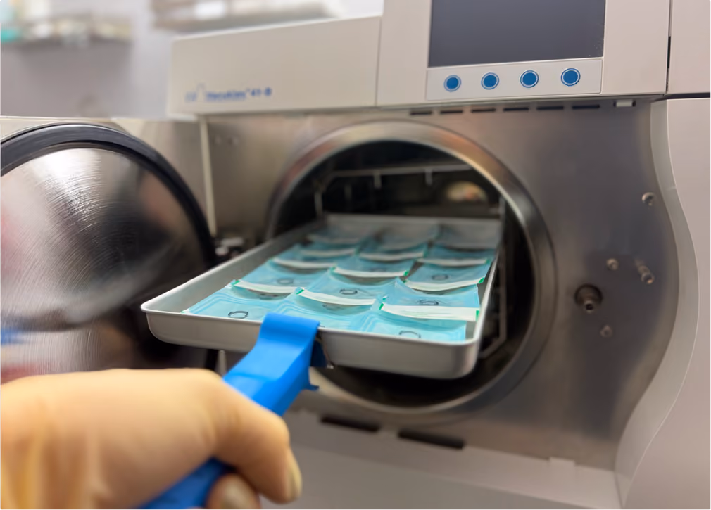 Behandschuhte Hand belädt den Autoklav mit Tablett steril verpackter Instrumente, Taboo Piercing Rostock