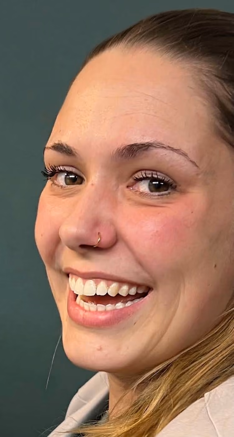 Lachende Kundin mit goldfarbenem Nostril-Ring vor dunkelgrüner Wand, Taboo Piercing Rostock