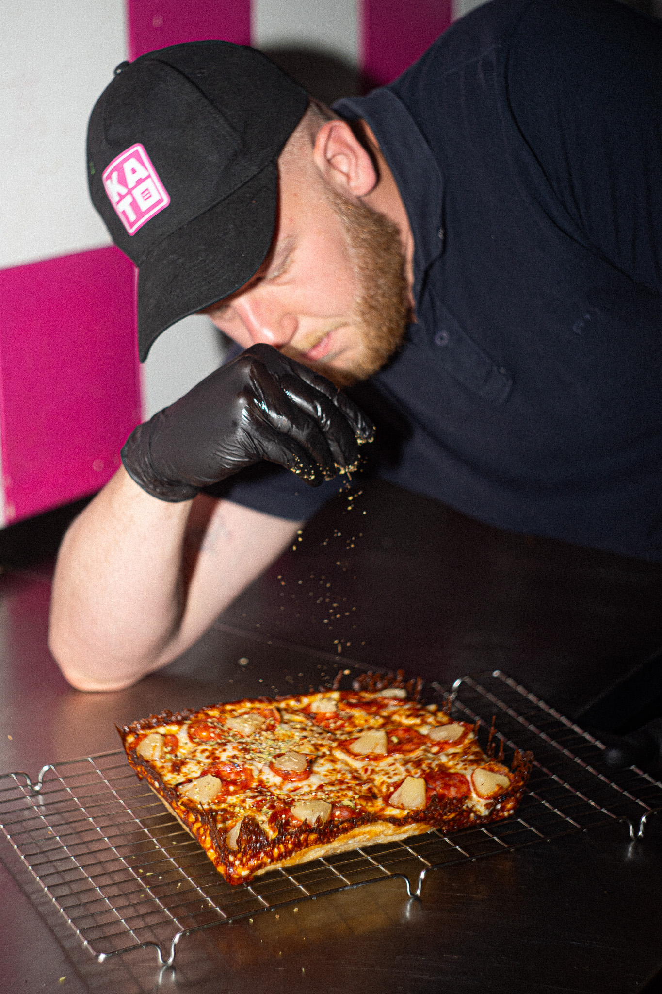 Pizzaiolo Kato Pizza posypuje upieczoną pizzę w stylu Detroit