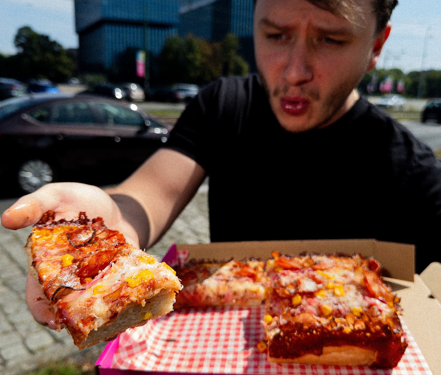 Klient z kawałkiem pizzy i pudełkiem Kato Pizza