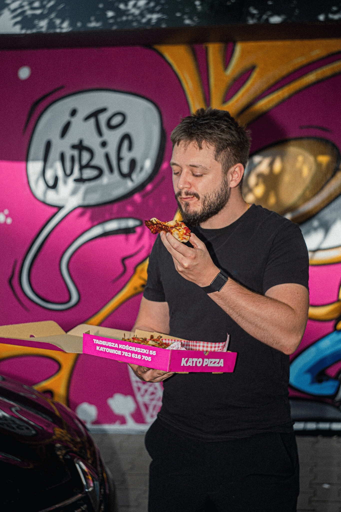 Klient je pizzę Kato Pizza na tle muralu „To lubię”