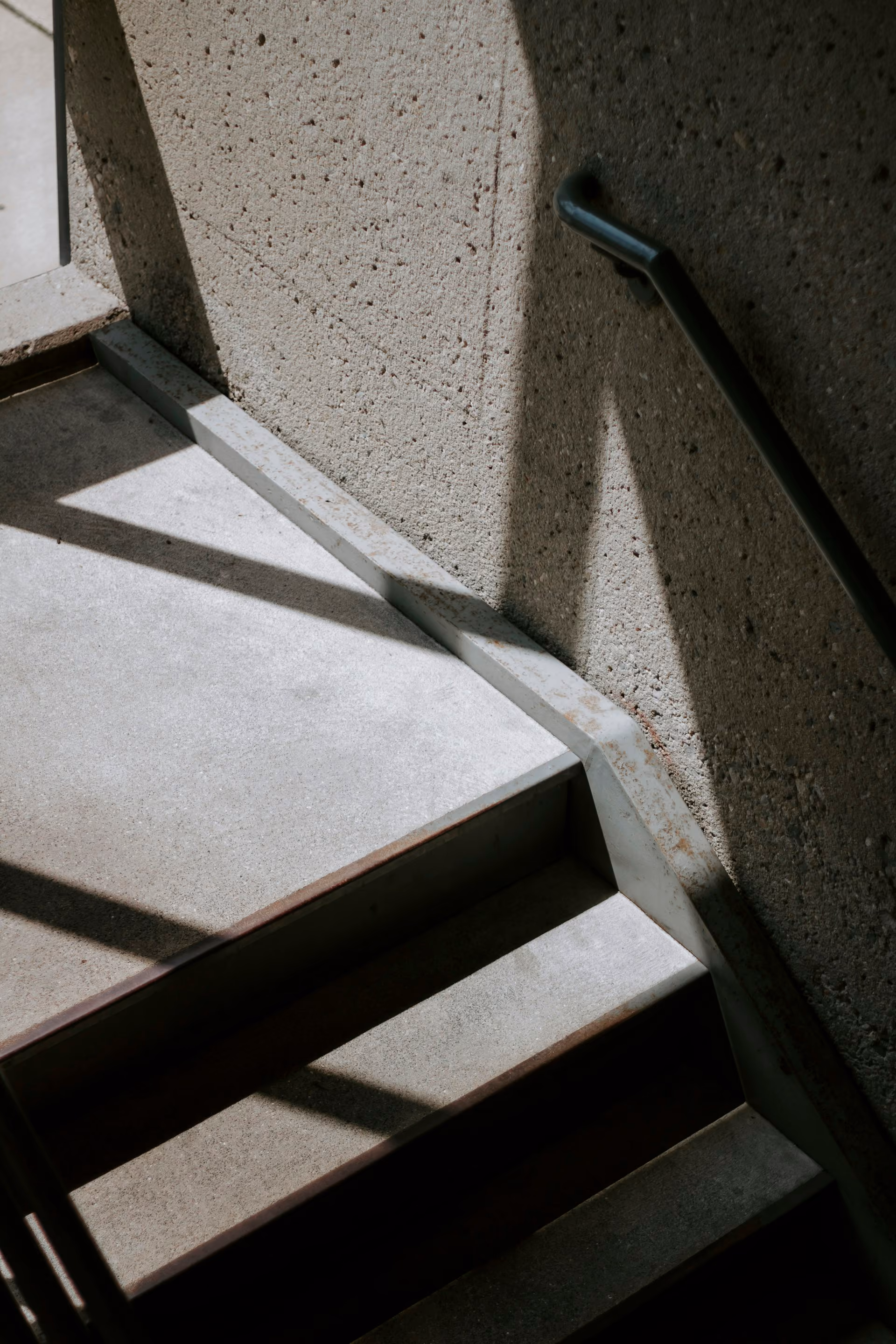 Close-up of a concrete stairwell corner with a worn steel handrail