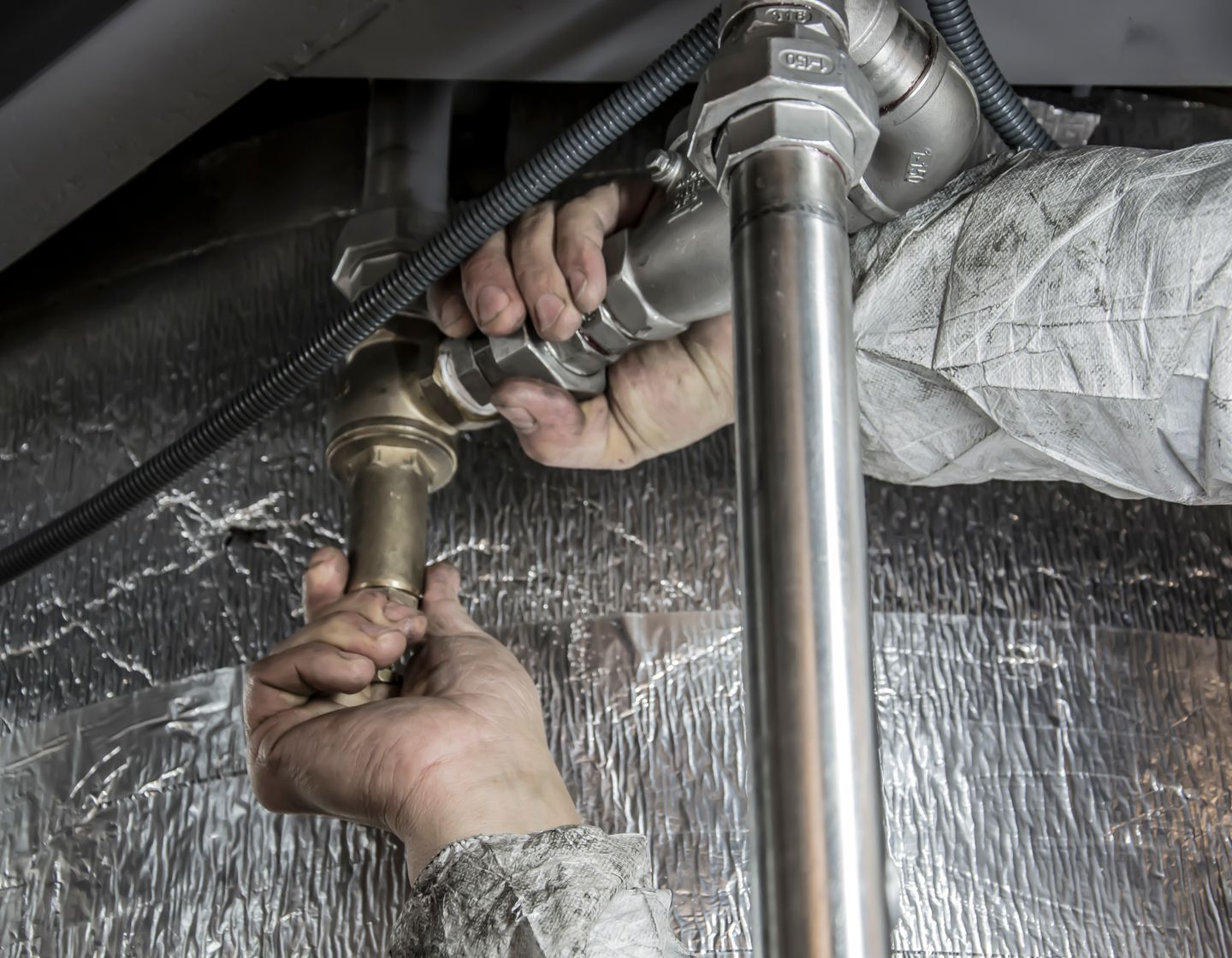 A plumber fitting brass and stainless supply pipework beneath a floor