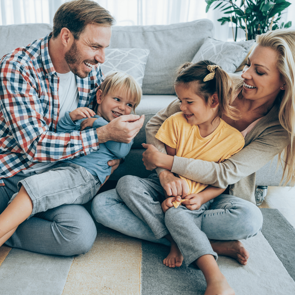 Vierköpfige Familie sitzt auf dem Wohnzimmerboden vor einem Sofa