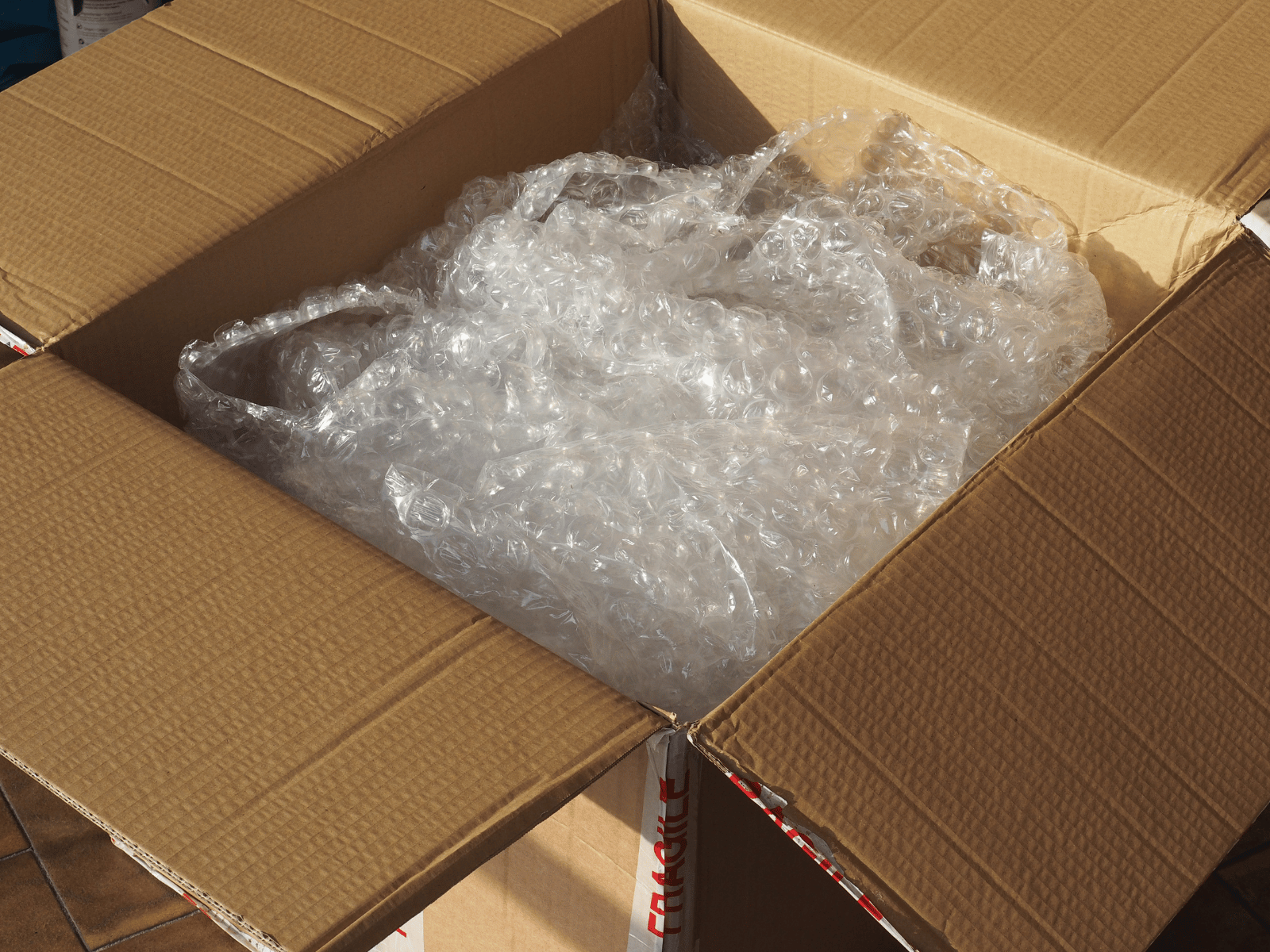 Offener Umzugskarton mit Luftpolsterfolie, daneben Klebeband mit der Aufschrift Fragile