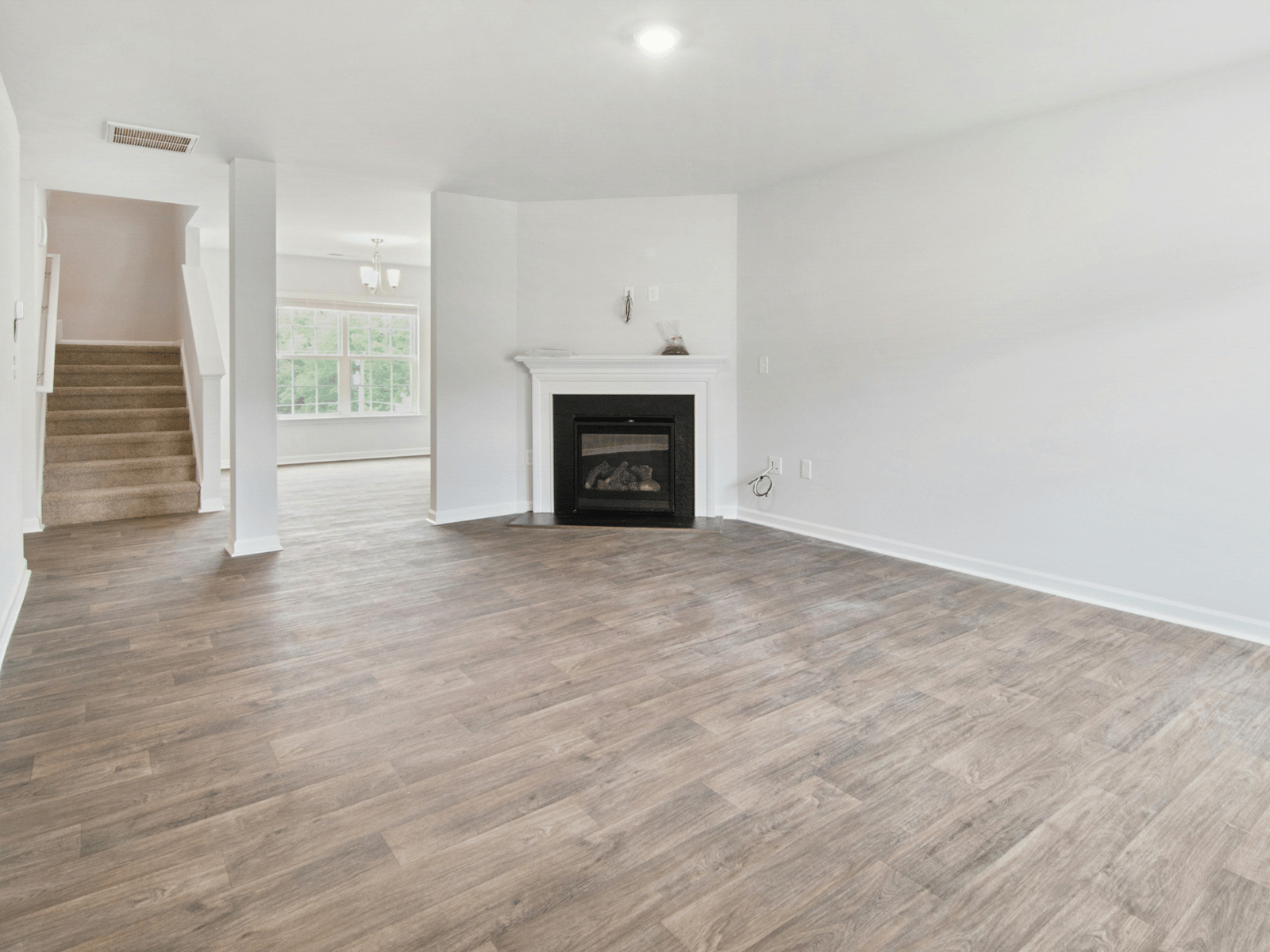 Leerer Wohnraum mit hellem Boden, Kamin und Treppe