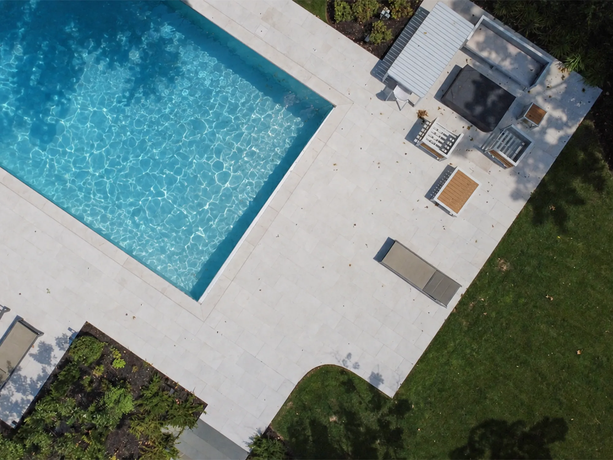 Overhead view of Tuscany Beige marble pavers along a pool edge beside outdoor seating and a lawn.