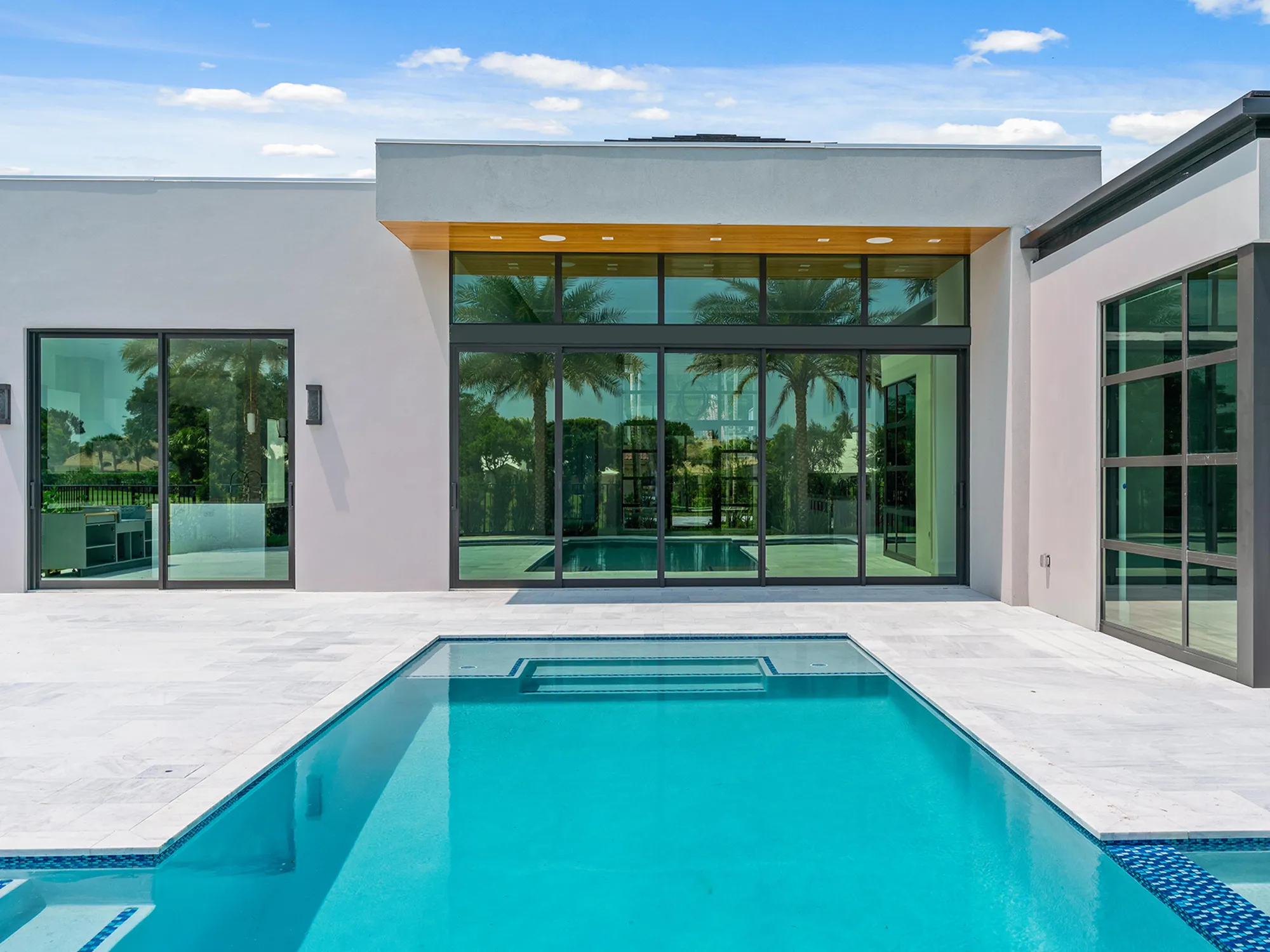 Ice White marble pavers around a rectangular swimming pool beside a modern home with large glass doors.