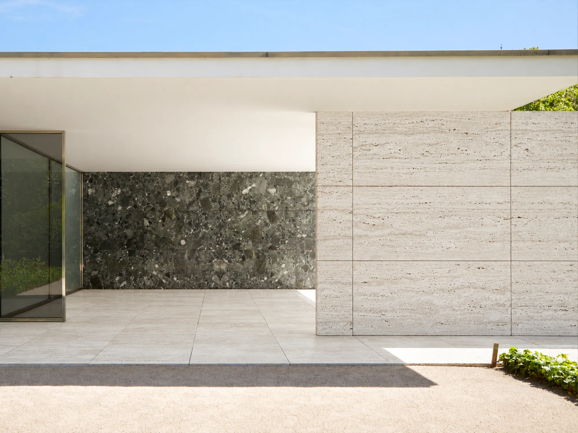 Ivory Travertine Vein Cut wall cladding and terrace flooring beneath a flat white roof, beside glass panels and a dark stone accent wall.