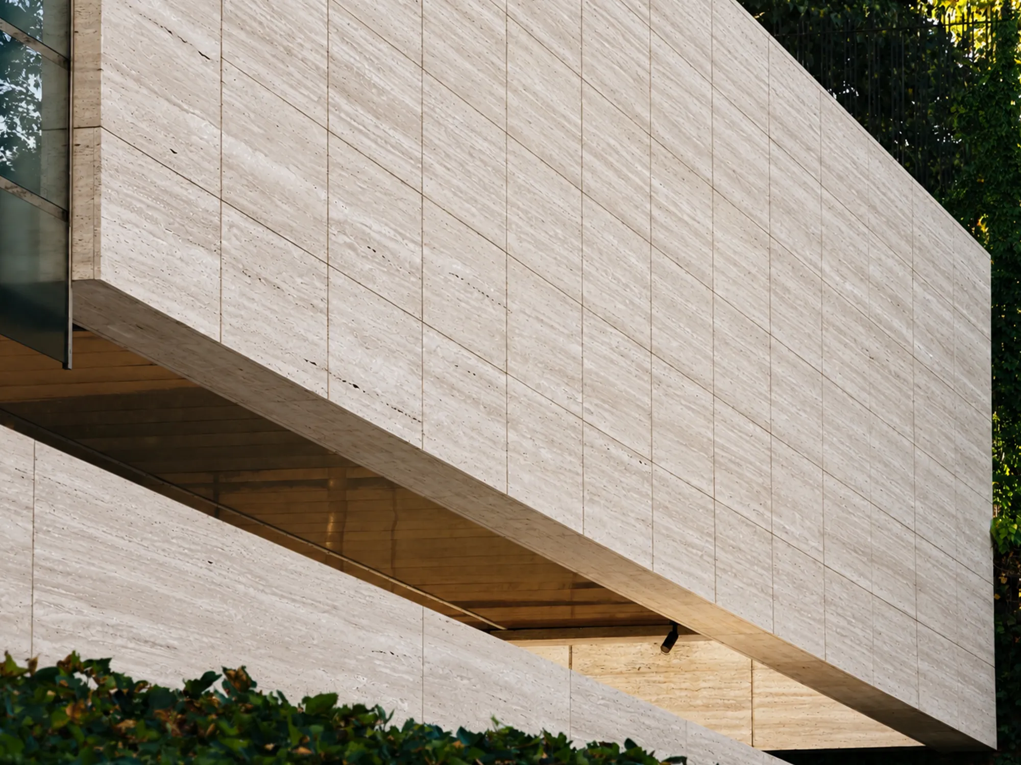 Ivory Travertine exterior wall panels with pale beige linear veining and rectangular joints beside glass and greenery.