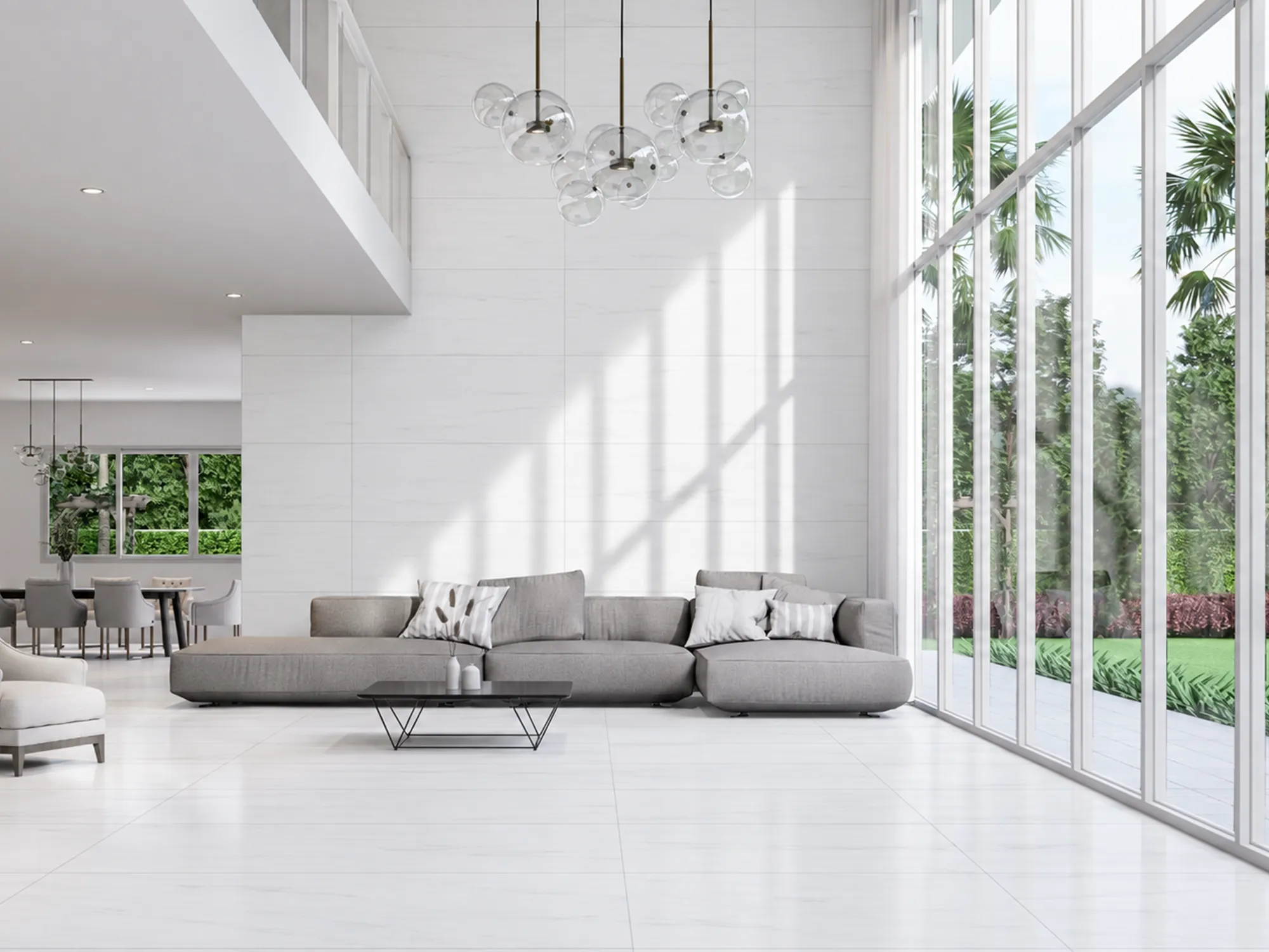 Bianco Dolomiti marble wall and floor tiles in a double-height living room with a gray sofa and tall sunlit windows.