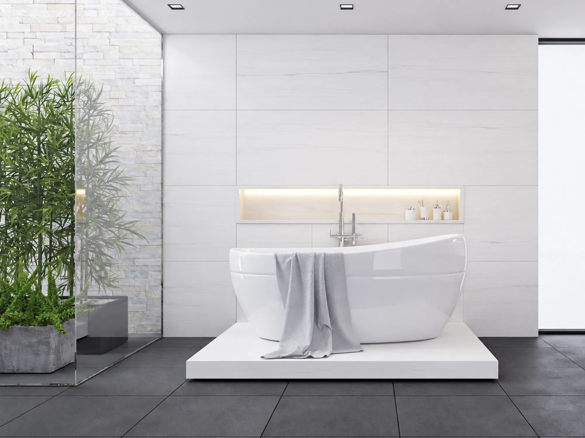 White marble wall tiles with subtle gray veining behind a freestanding bathtub, with an illuminated wall niche.