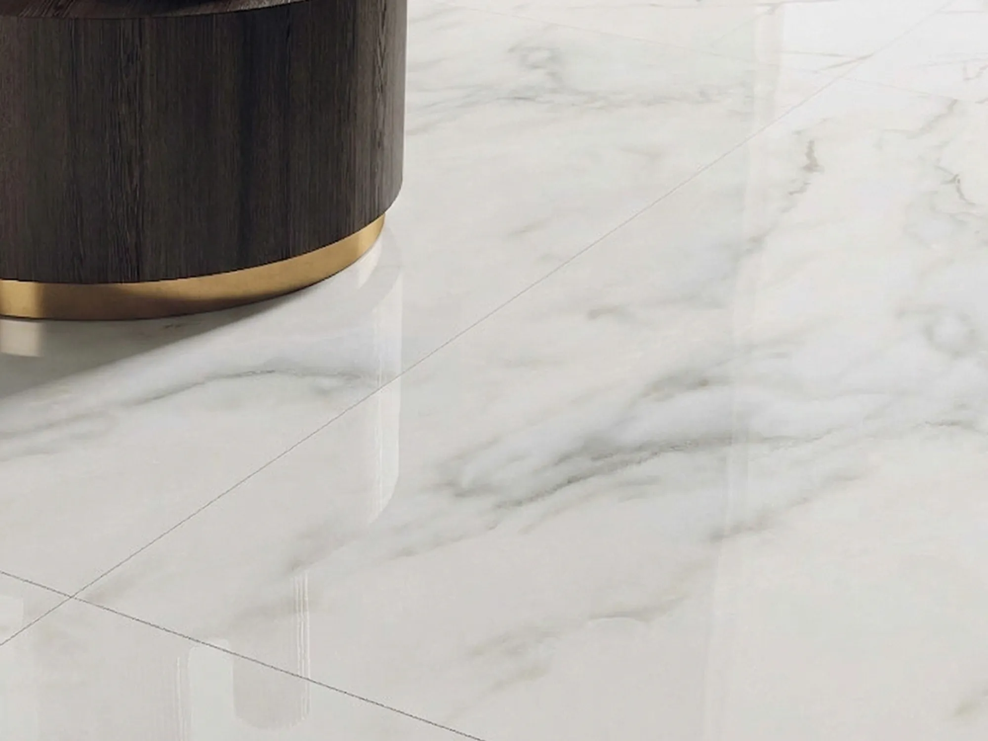 Close-up of Calacatta Green marble floor tiles with flowing gray veins beside a dark wood table base with brass trim.