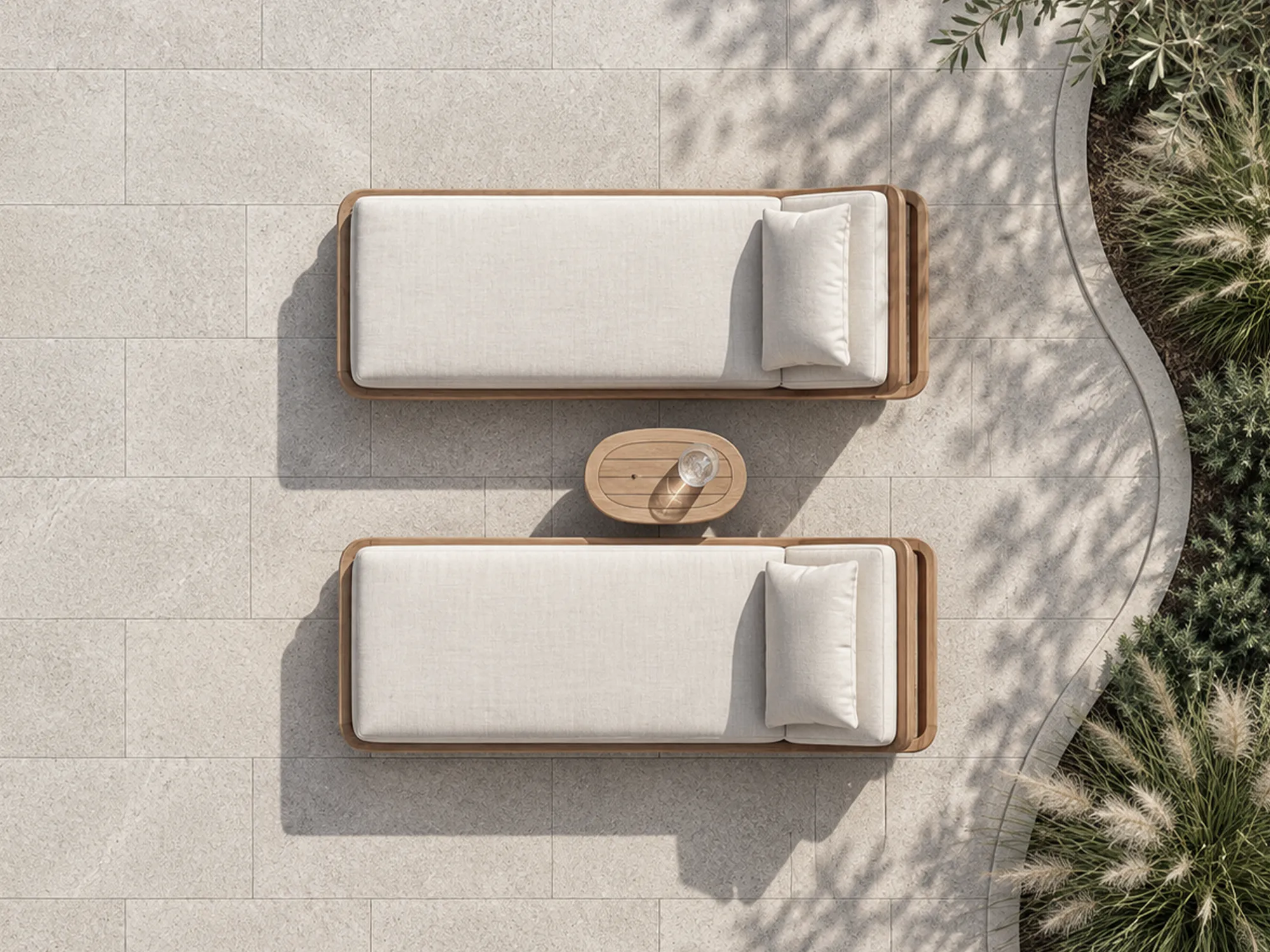 Overhead view of light beige natural stone pavers with two cushioned wooden loungers beside a curved garden bed.