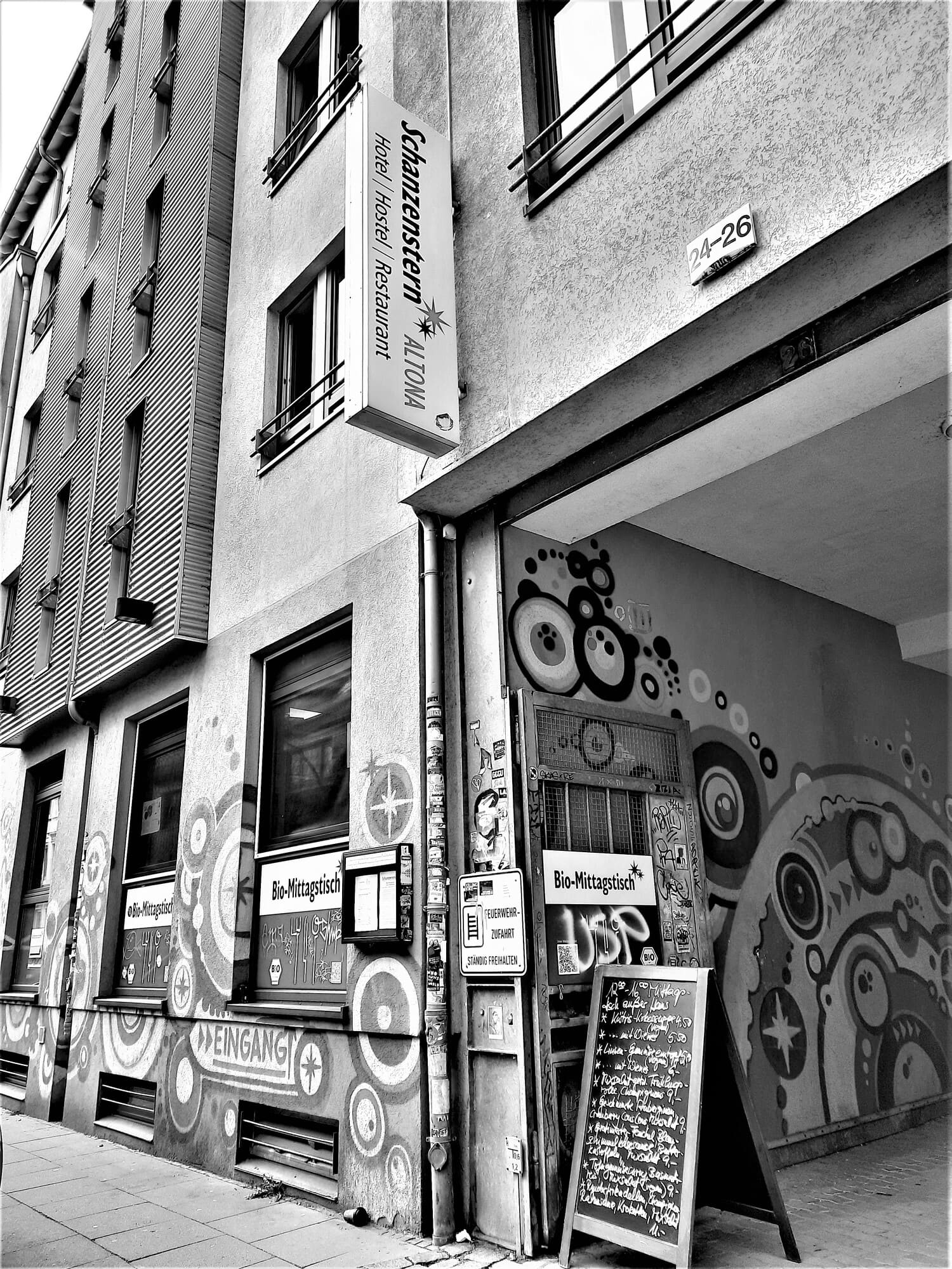 Schwarz-Weiß-Aufnahme einer Straßenfassade mit Graffiti und offenem Hauseingang