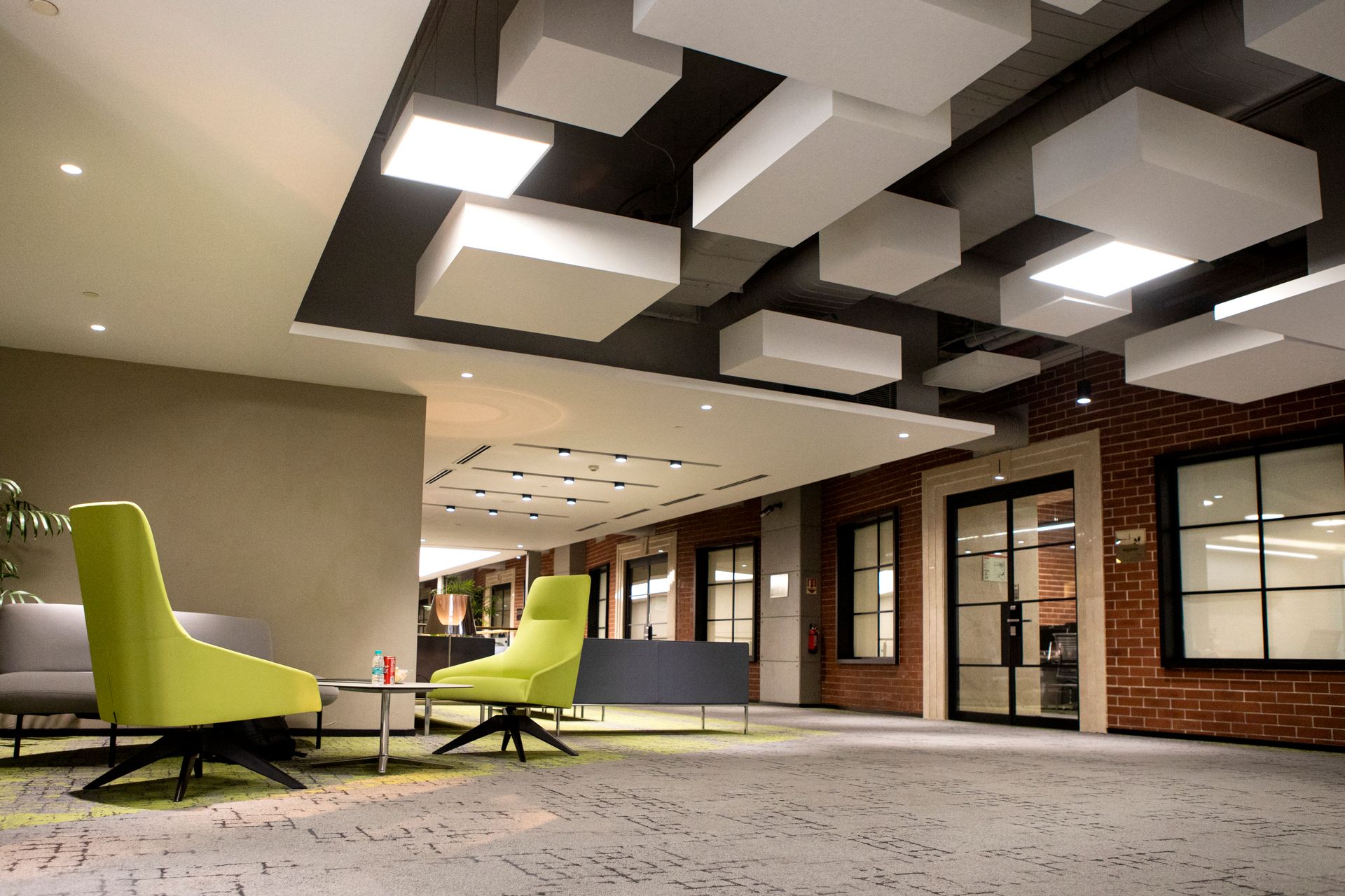 Office lounge beneath suspended acoustic ceiling panels with green armchairs