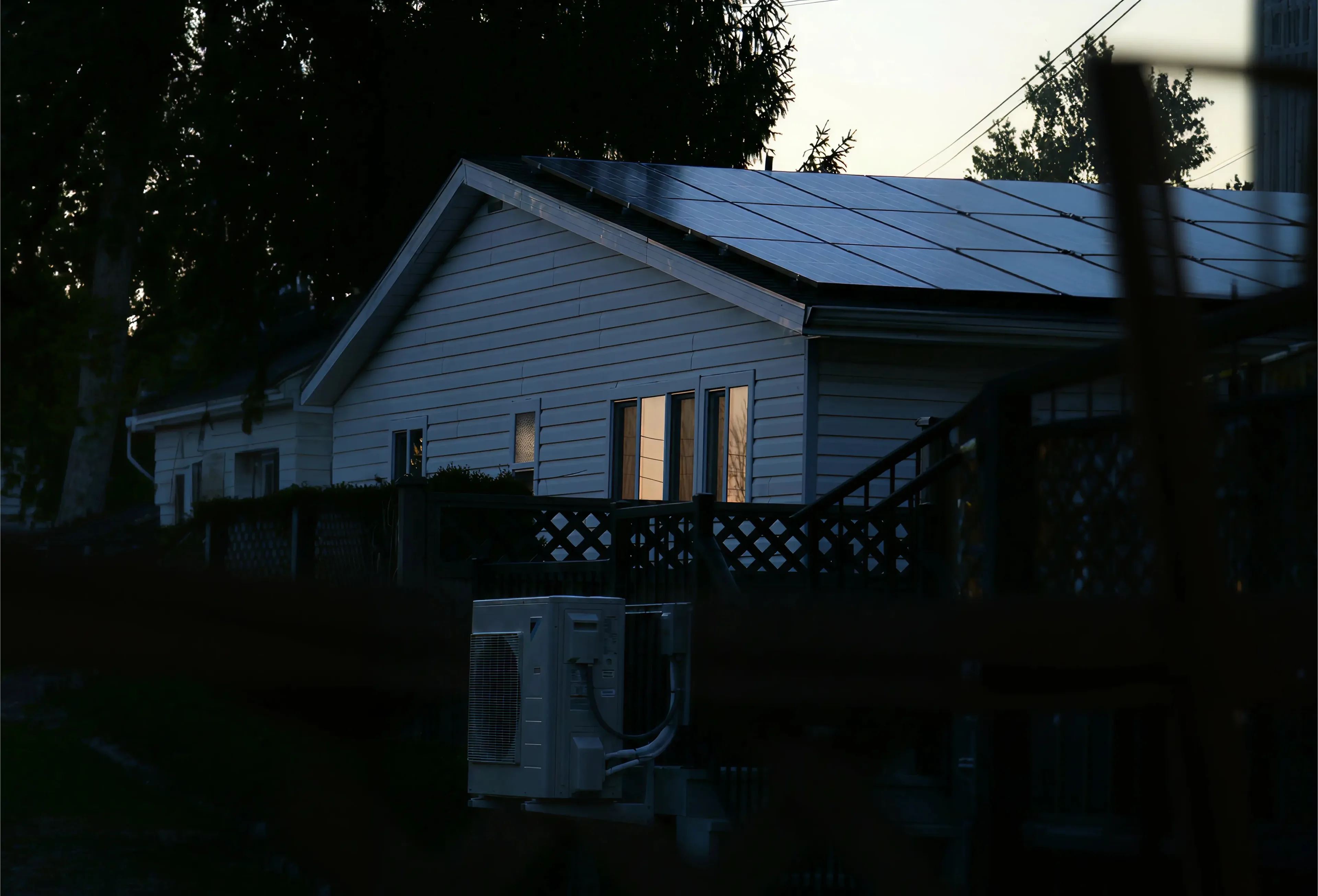 White house with solar panels on the roof and windows reflecting sunset light at dusk.