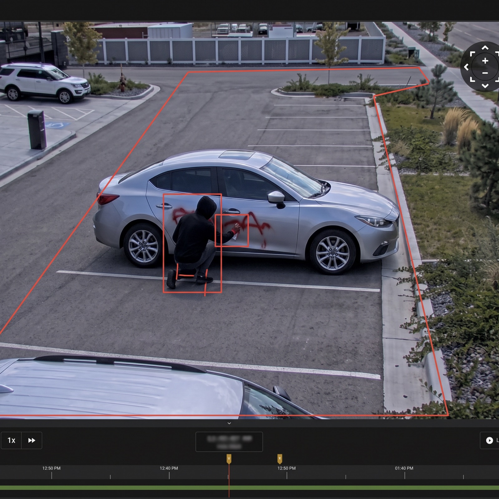 Overhead footage zoomed in on a hooded figure crouched at the door of a silver car, outlined by a red detection box.