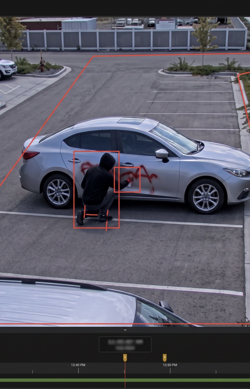 A recorded event: a hooded figure spray-painting a parked car, with the detection box and tripwire that triggered it.