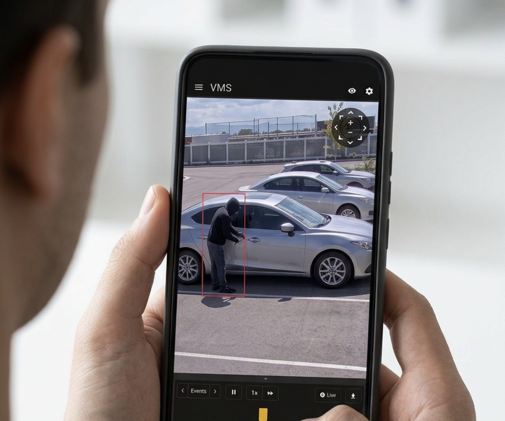 Live footage on a phone, showing a figure beside a parked car picked out by a red detection box.