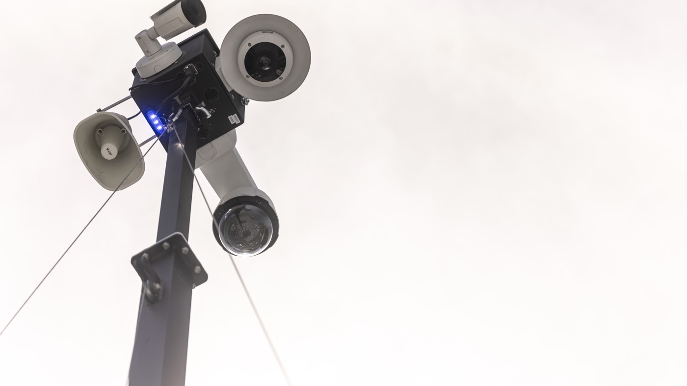 The camera head and loudspeaker horn against an open sky, blue beacon lit.