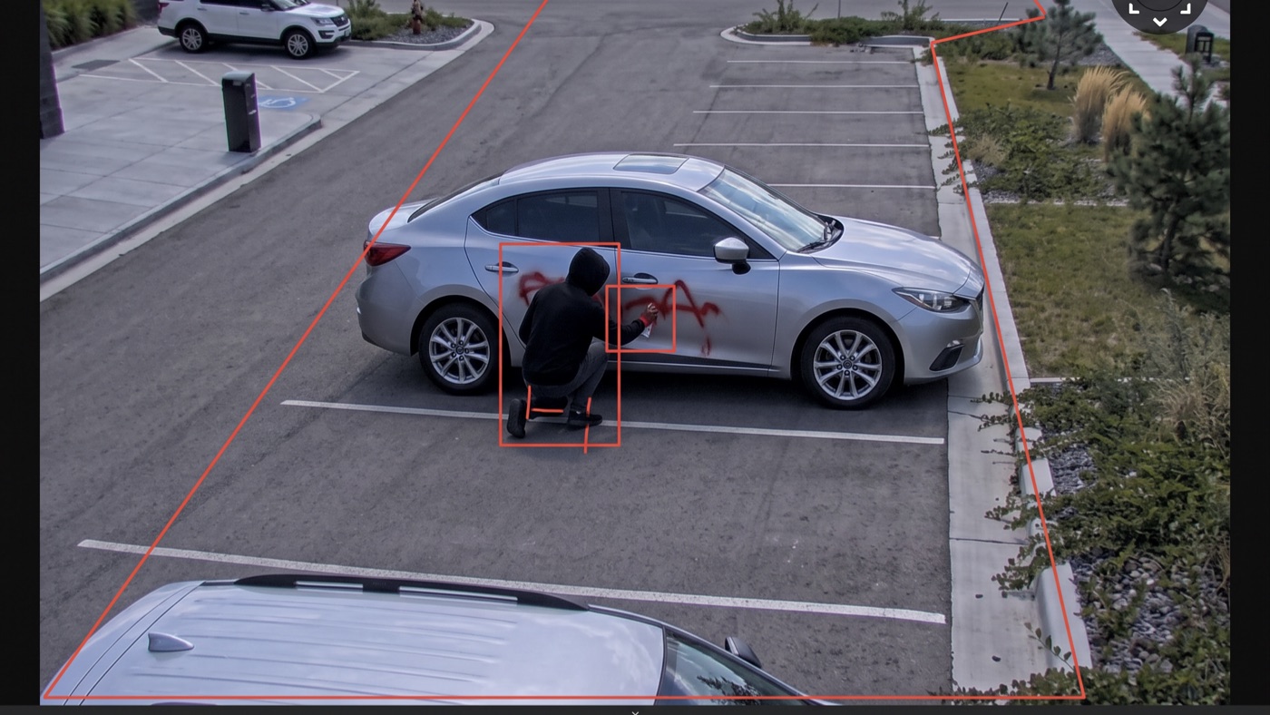 Overhead footage of a hooded figure spray-painting a parked car, caught by the detection box and tripwire.