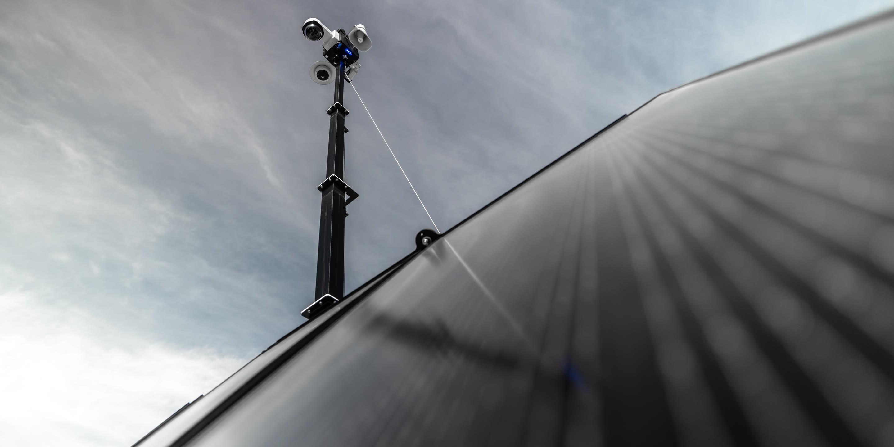 Looking up the mast of a Deploy unit past its solar panel to the camera head against the sky.