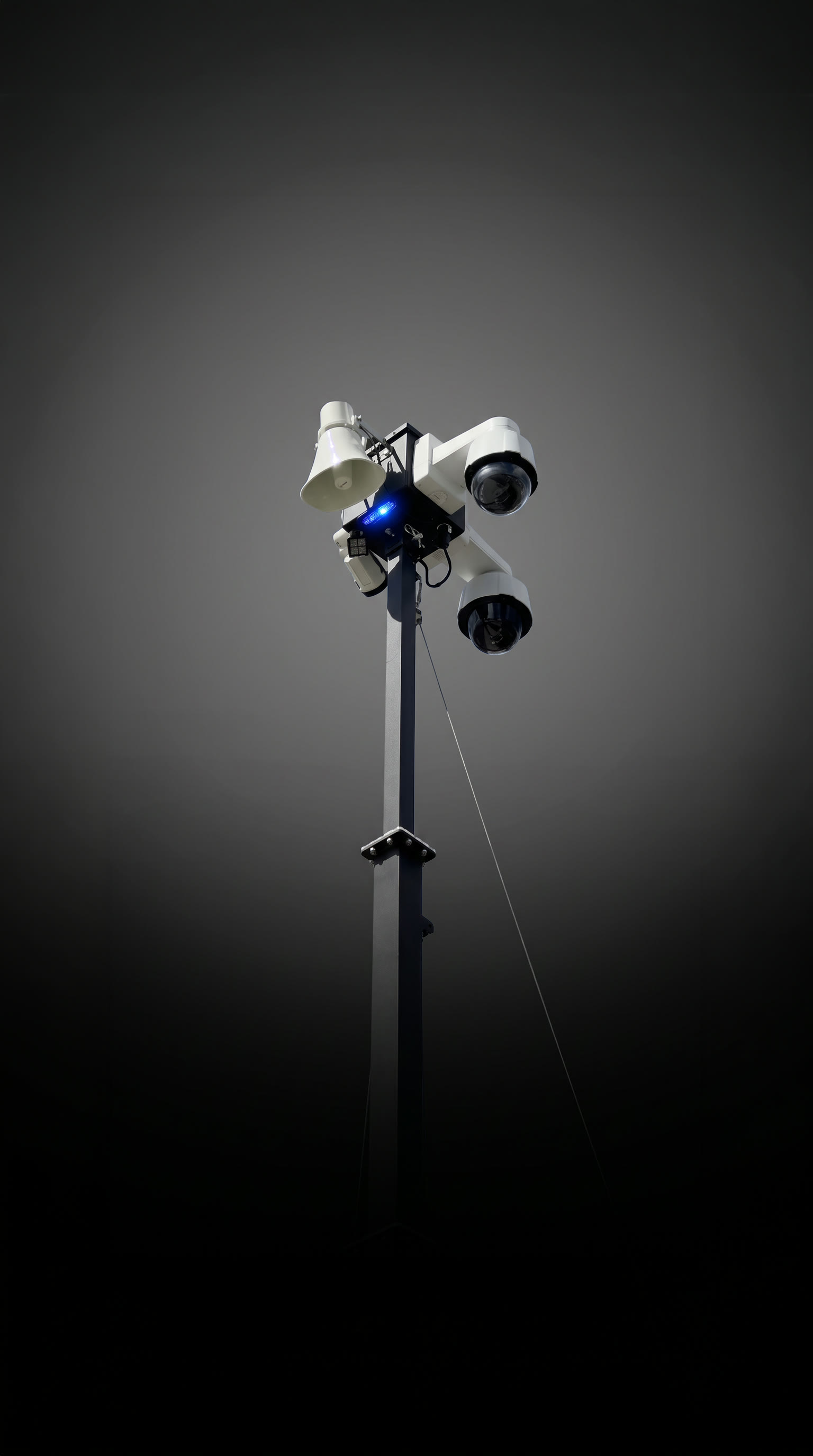 The camera head on its mast: two dome cameras, a loudspeaker horn and the blue beacon, against a dark backdrop.