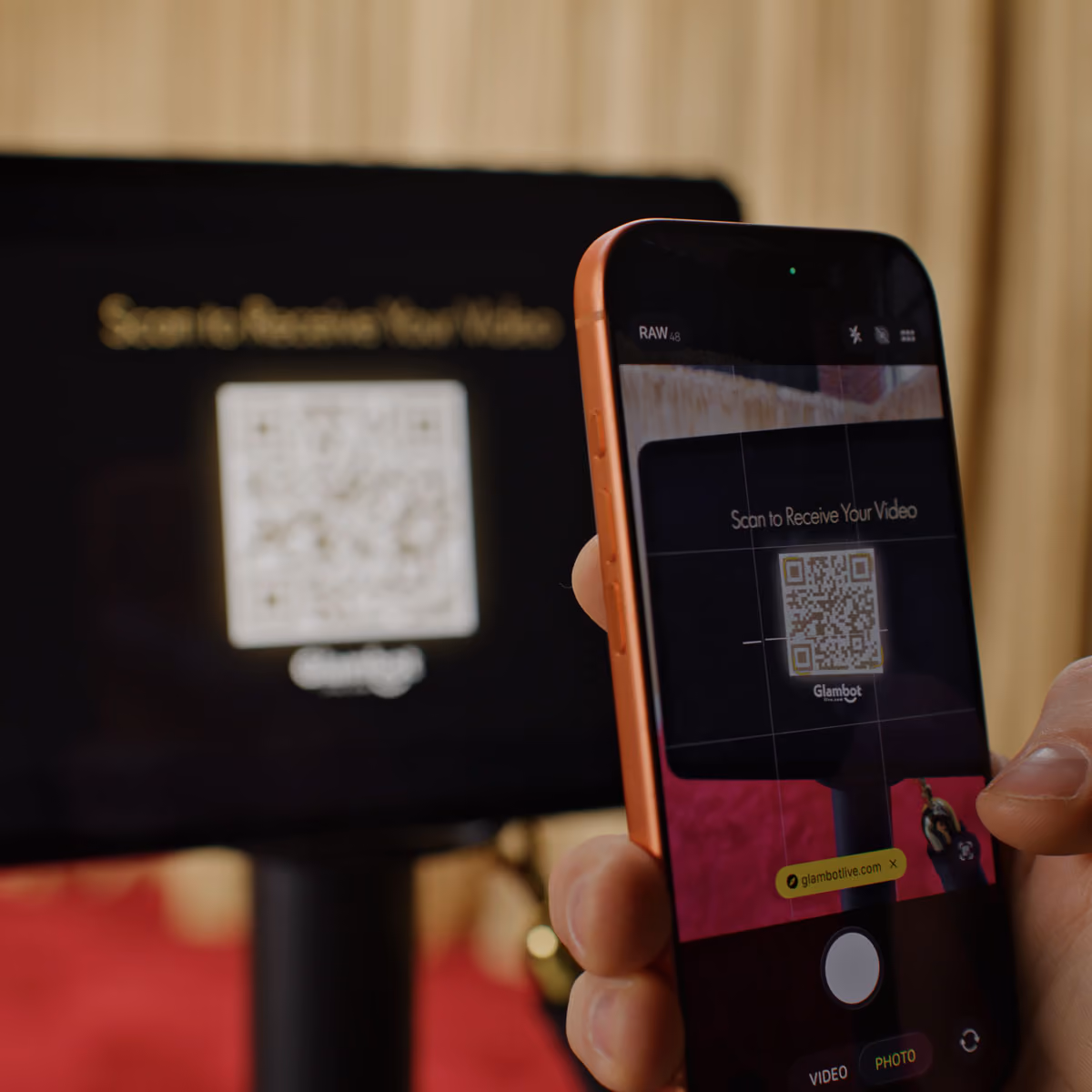 Close-up of a hand holding a smartphone scanning a QR code on a screen with the text 'Scan to Receive Your Video' displayed above the QR code.