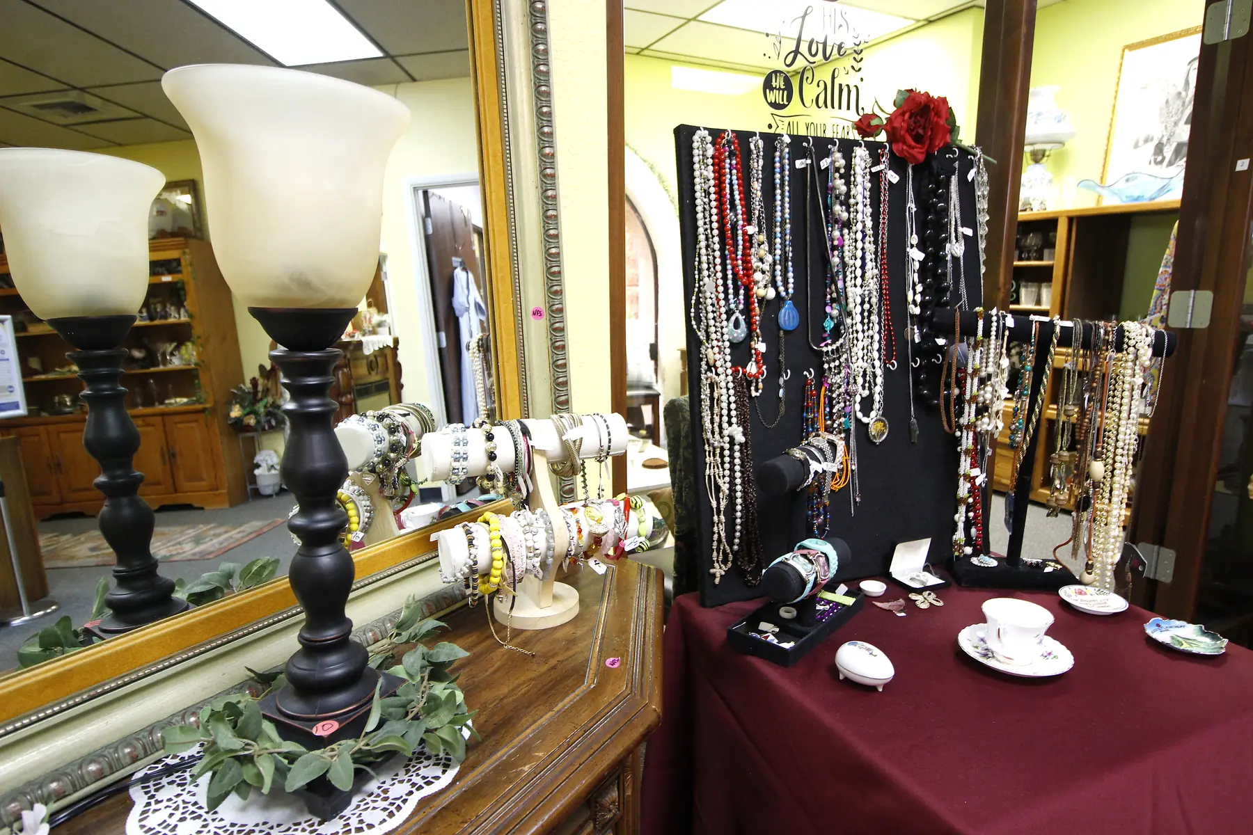 Necklaces, bracelets and vintage lamps arranged on a display table at Glorious Treasures Thrift Store