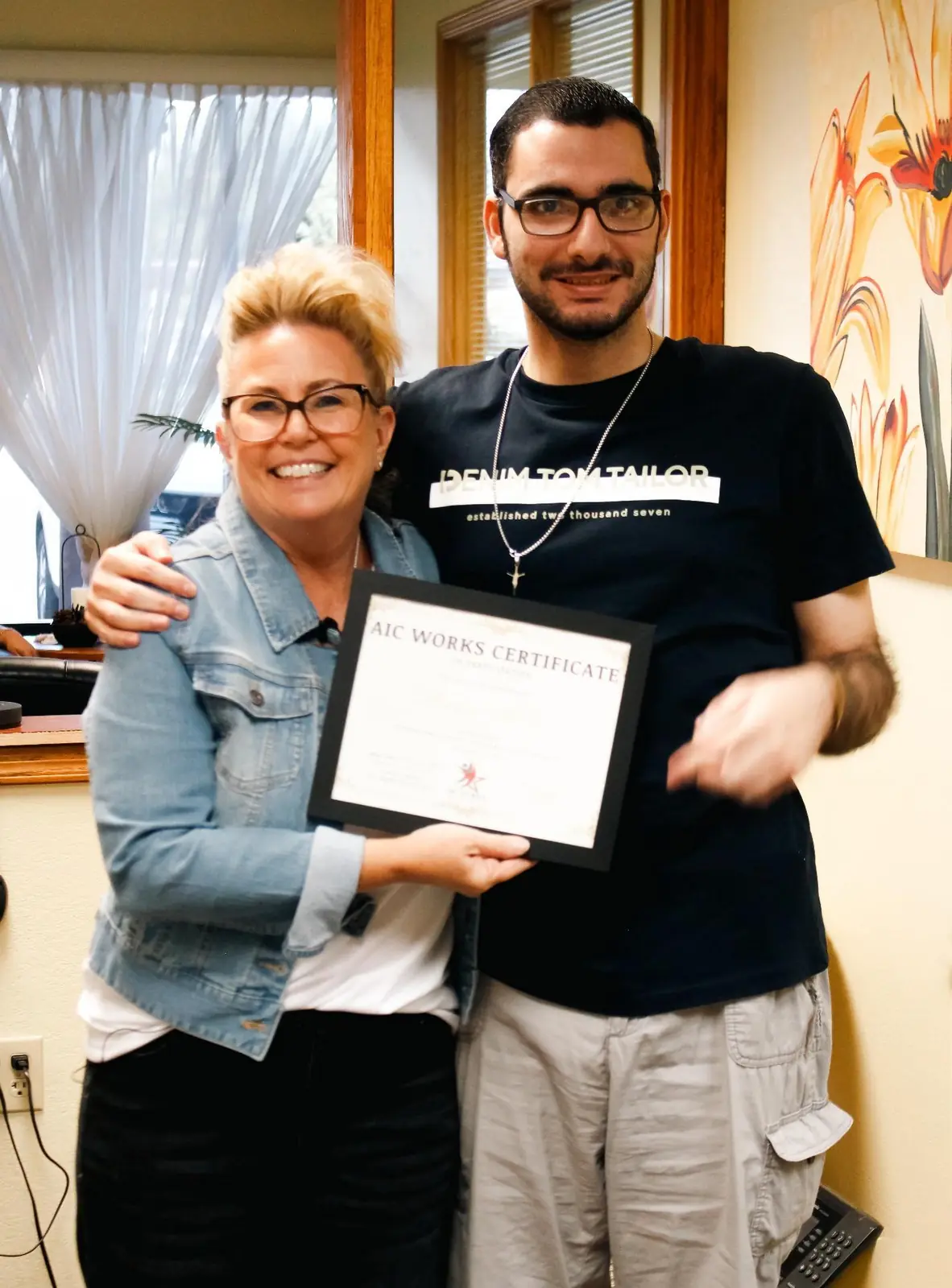 An AIC WORKS graduate and an AIC staff member hold his Certificate of Completion together, arm in arm