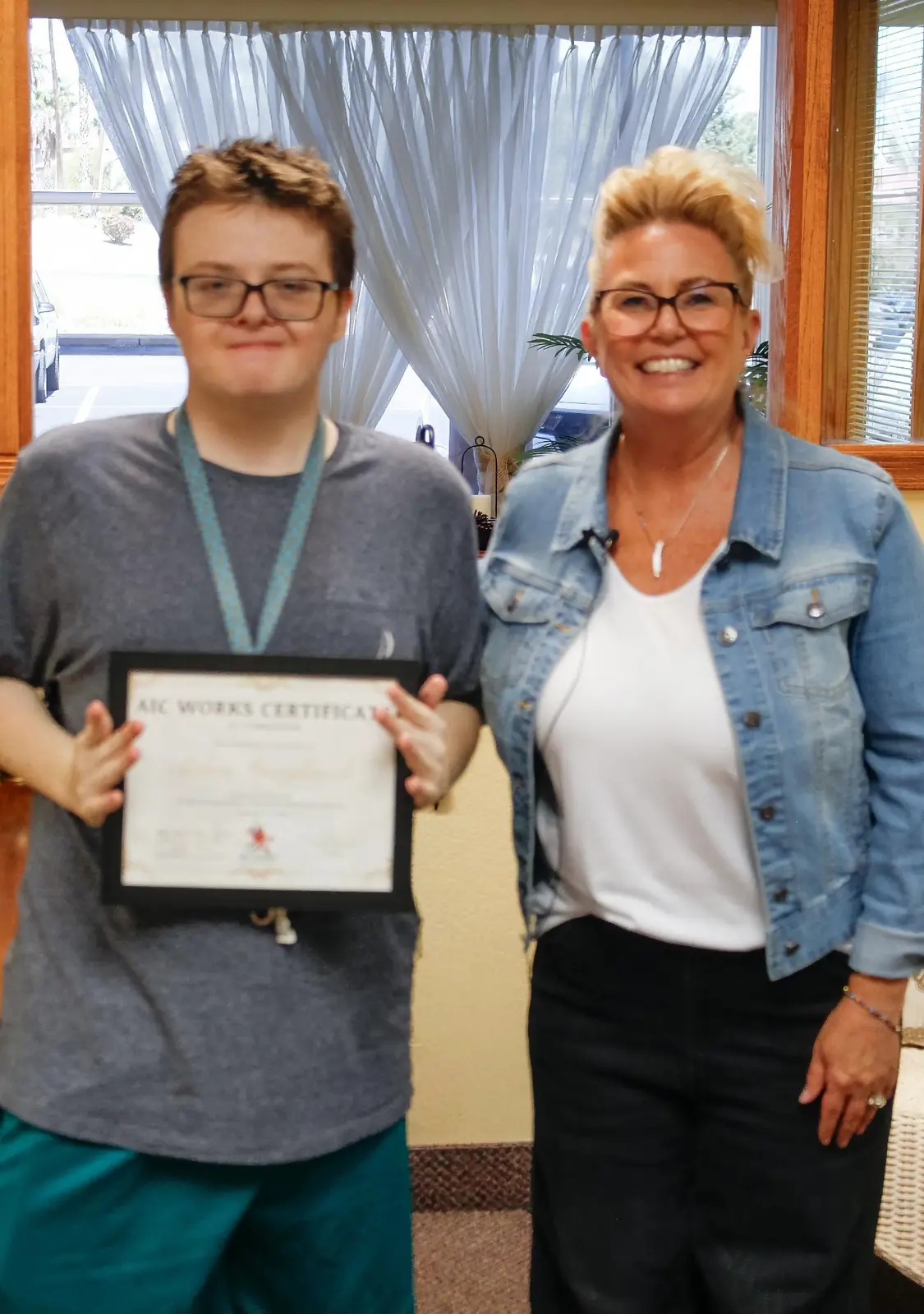 A smiling AIC WORKS graduate holds his Certificate of Completion beside an AIC staff member