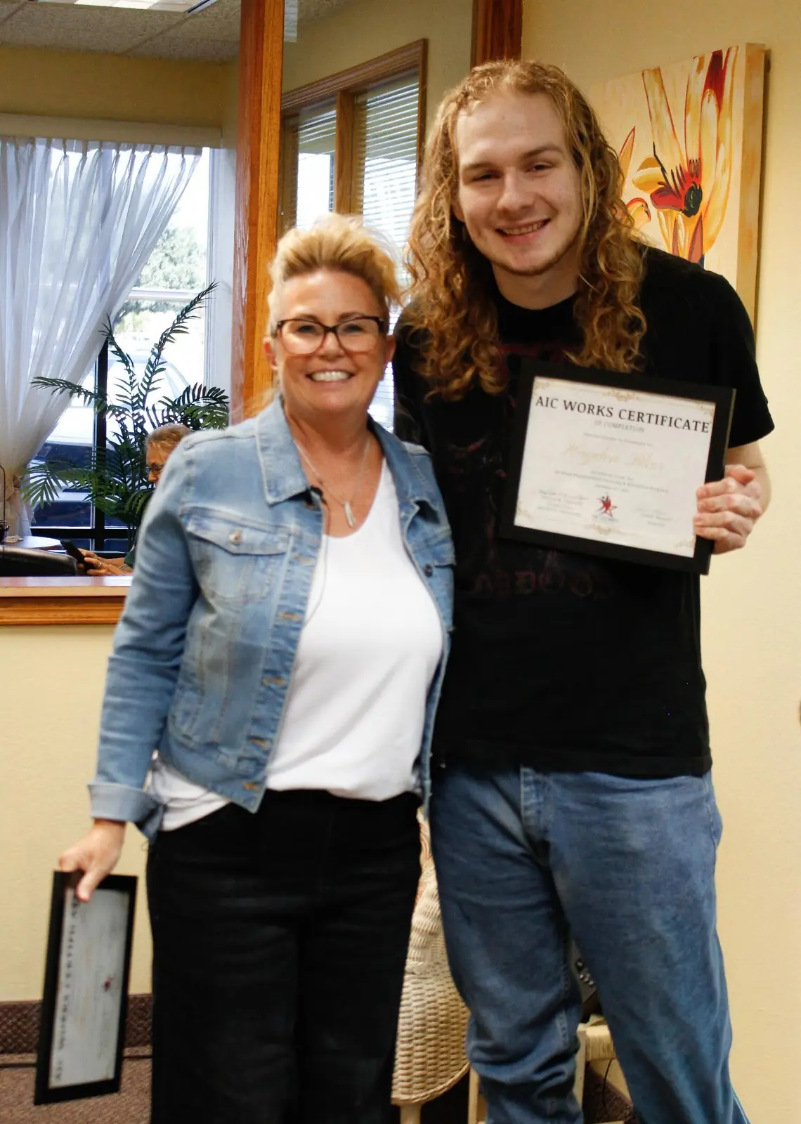 A smiling AIC WORKS graduate shows his certificate while standing with an AIC staff member