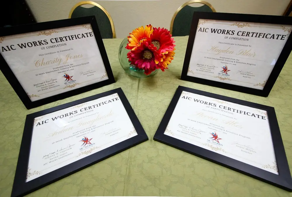 Four framed AIC WORKS Certificates of Completion arranged around a bright flower centerpiece on graduation day