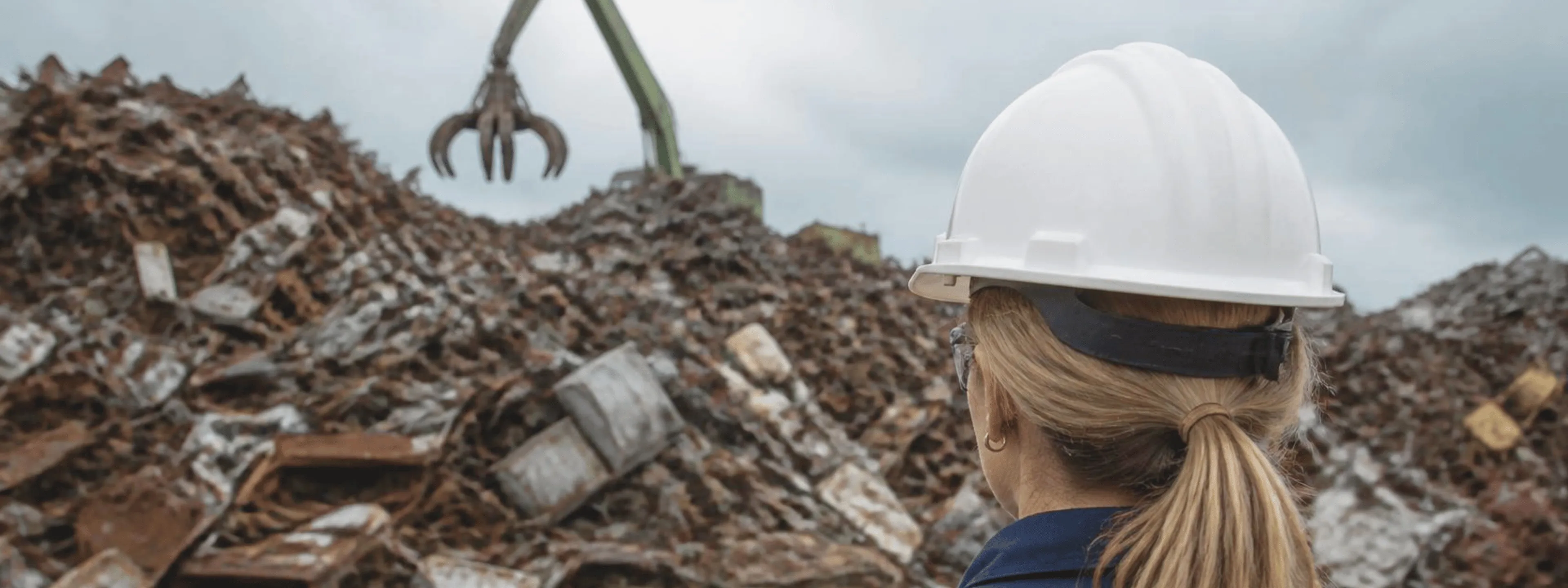 Operator in a white hard hat overlooking a scrap metal yard with a grapple crane