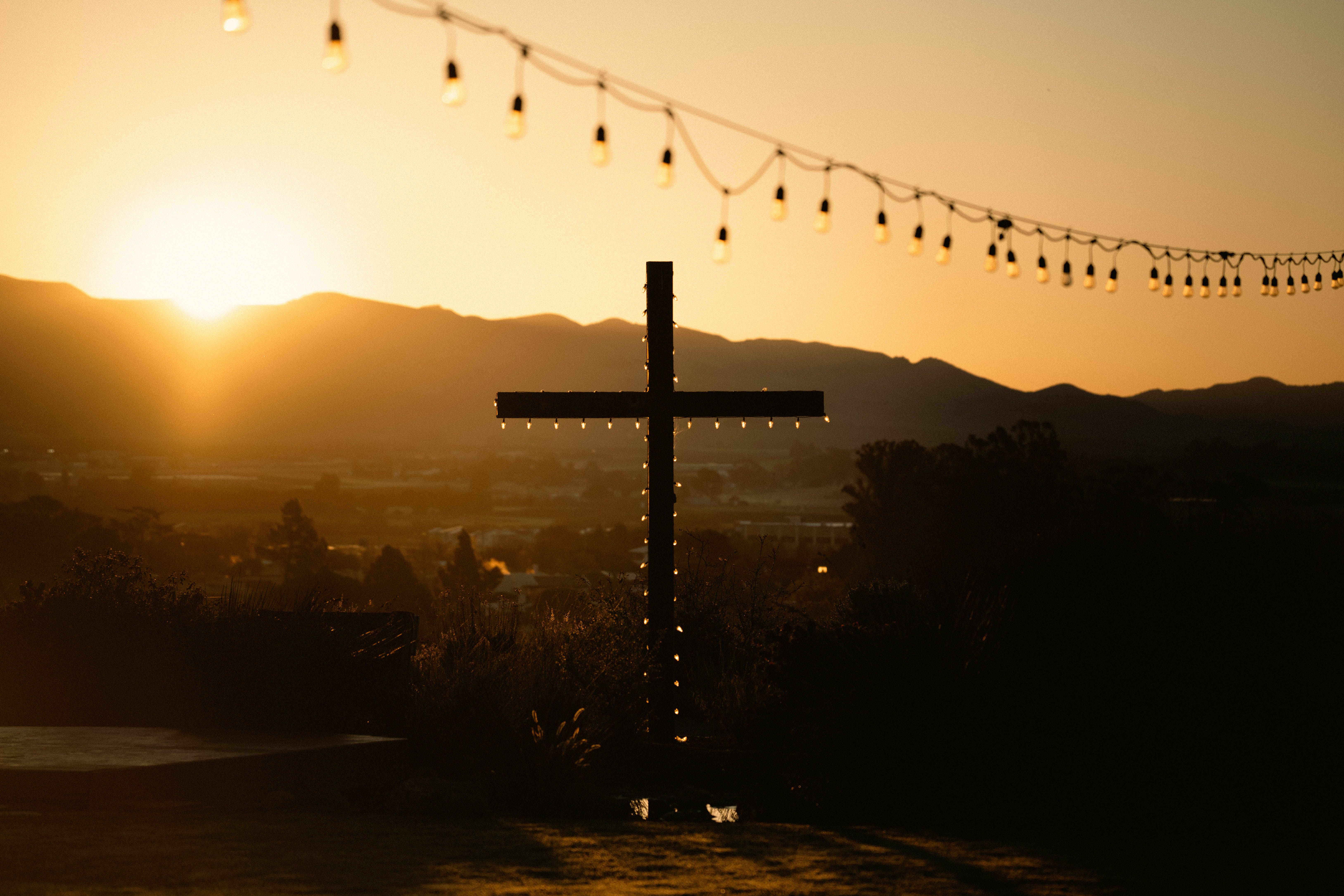 A cross strung with lights on a hilltop at sunset