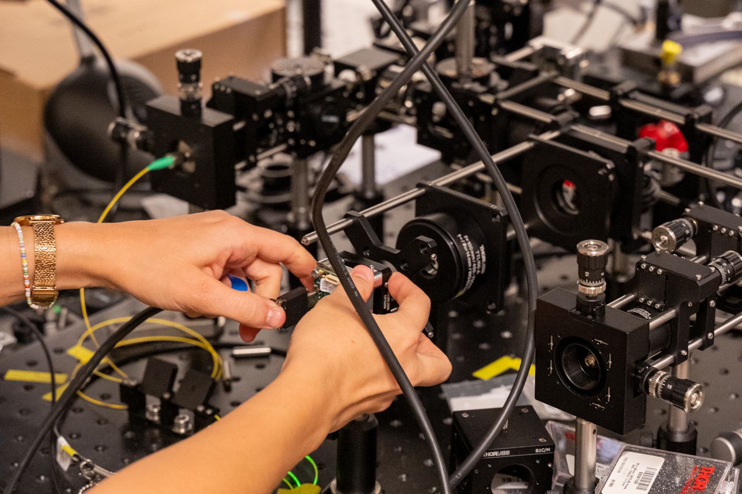 Two hands connecting a fibre patch cord on the optical characterization bench.