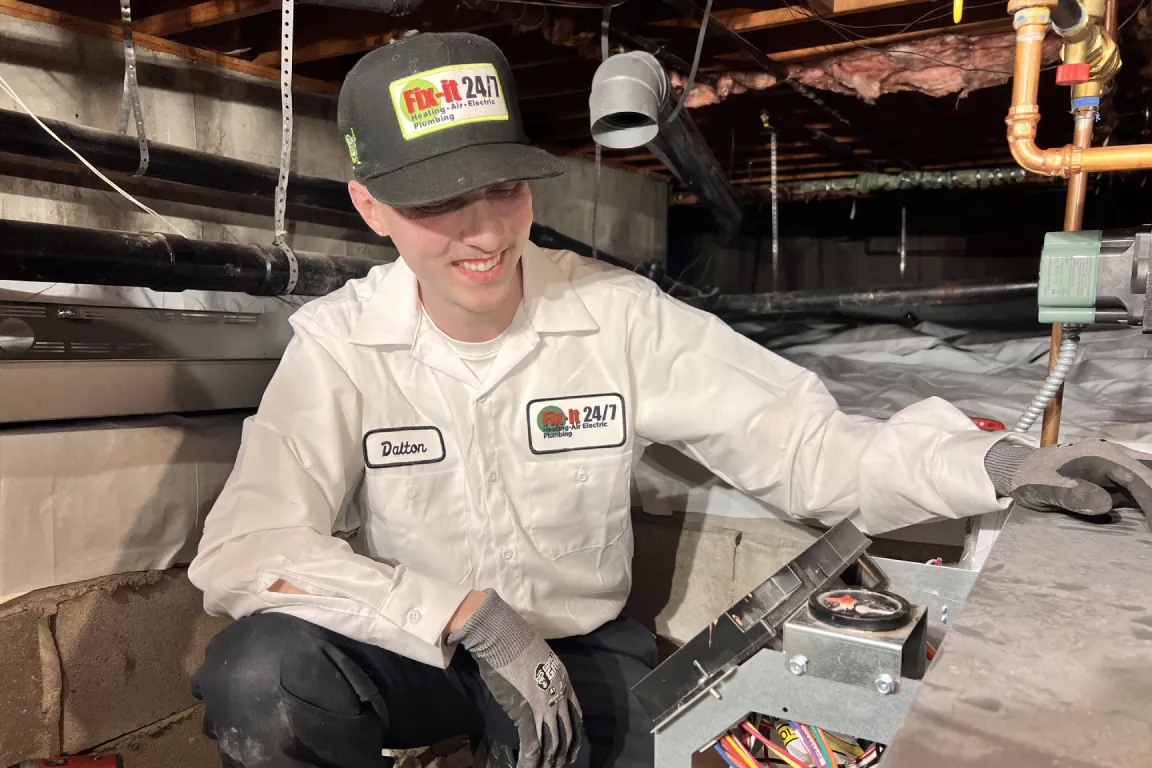 HVAC technician servicing an electrical component inside a heating and cooling system.
