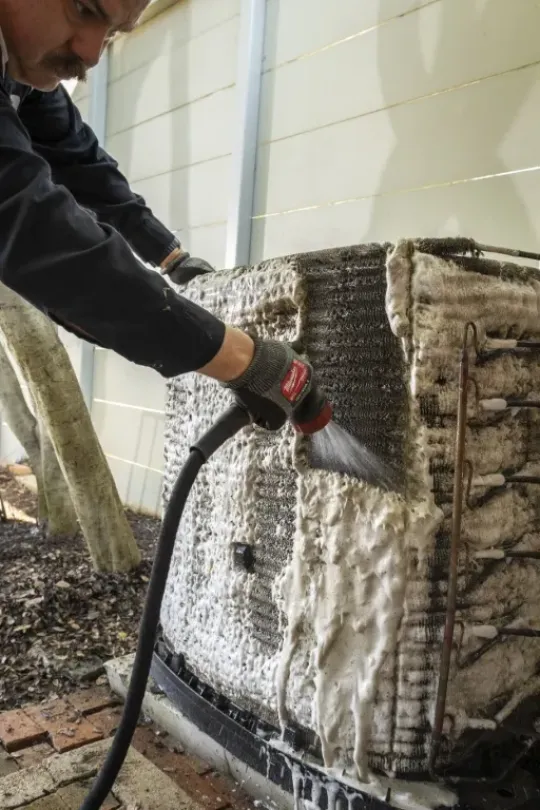 A technician working on cleaning an AC unit.