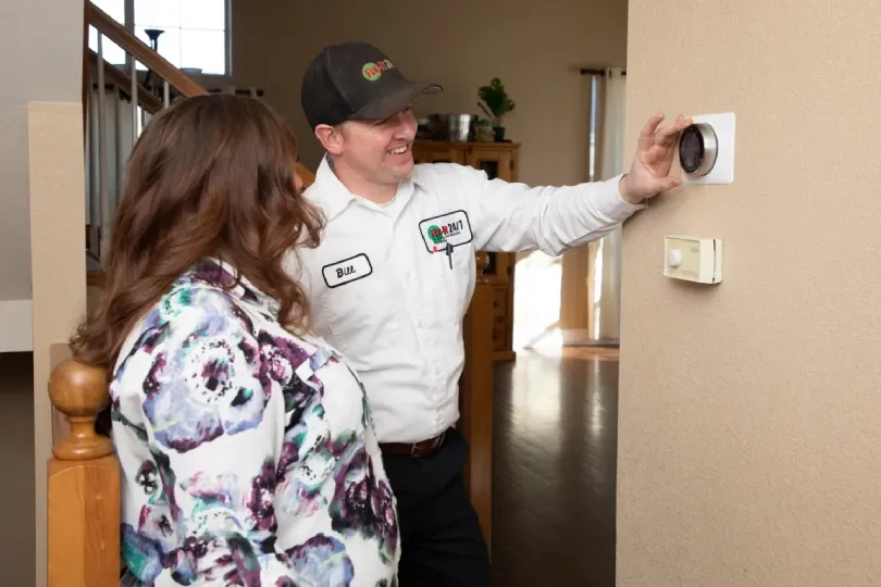 A technician showing a homeowner how a new thermostat works.