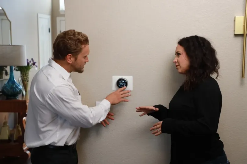 A customer and a technician talking next to a thermostat.