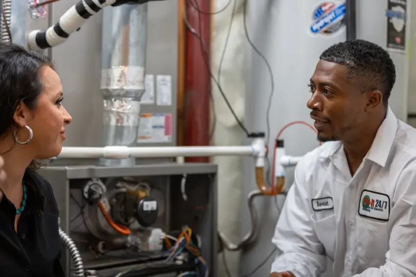 A technician speaking to a customer in front of a furnace.