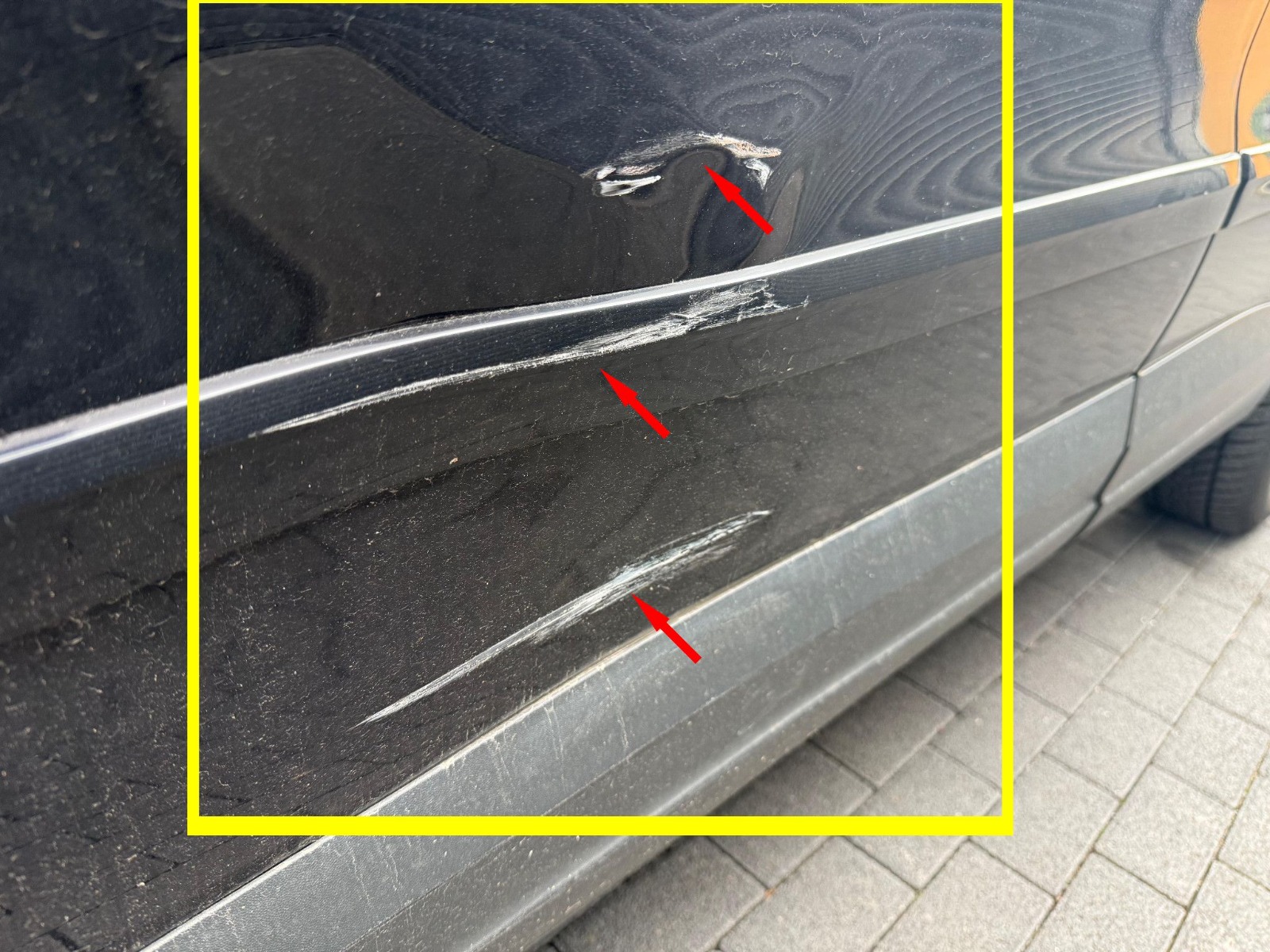 Markierter Seitenschaden an einer dunklen Fahrzeugkarosserie.