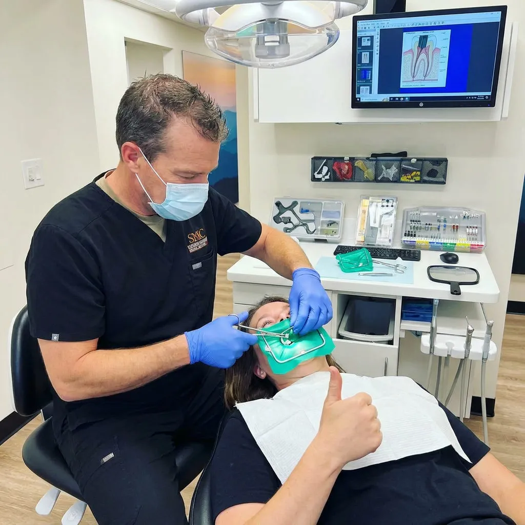 A dentist at Muldoon Dental Arts in Anchorage, AK, adjusts a rubber dam while a reclined patient gives a thumbs up.