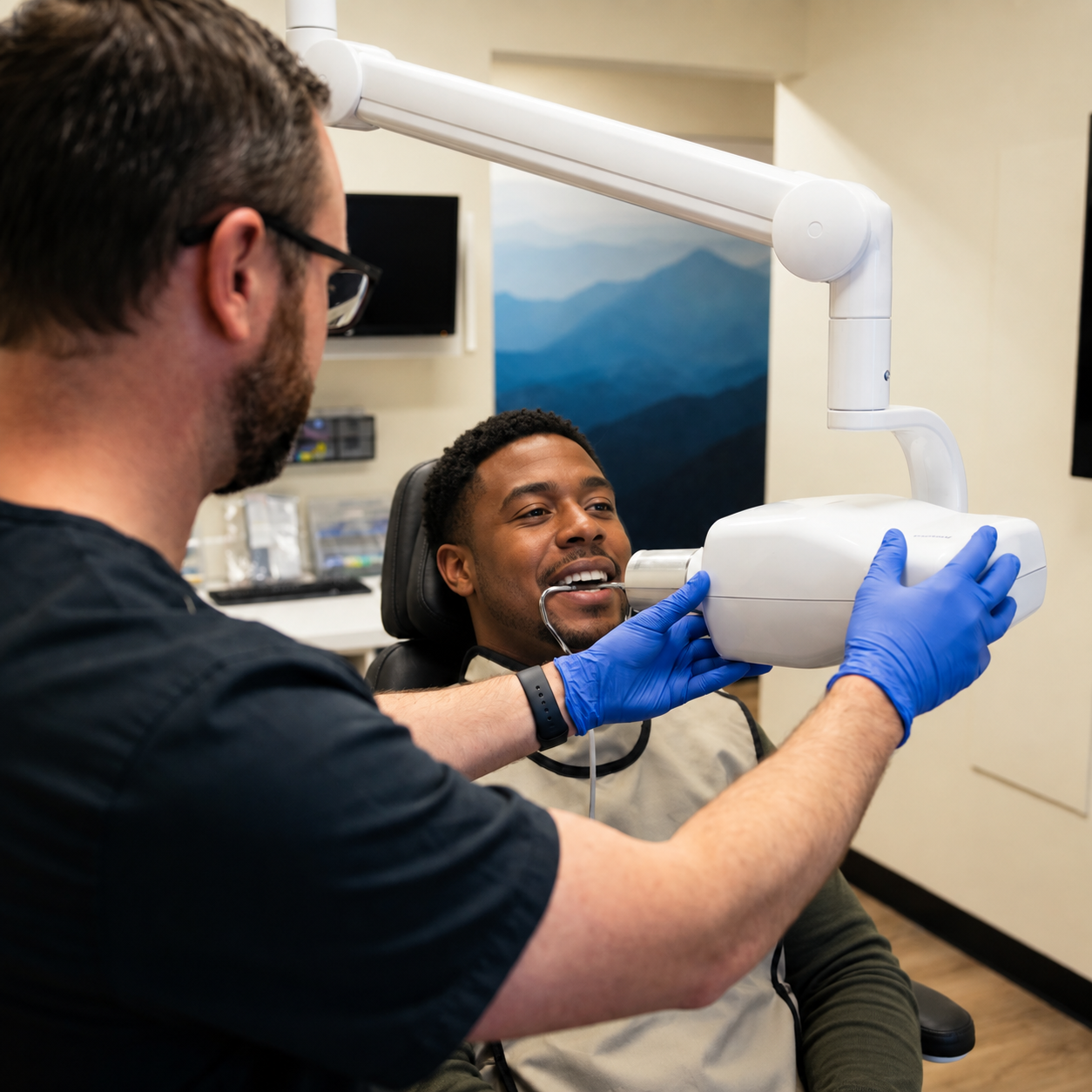 Dr. Anderson positions an X-ray unit for a patient wearing a protective shield during a dental exam.