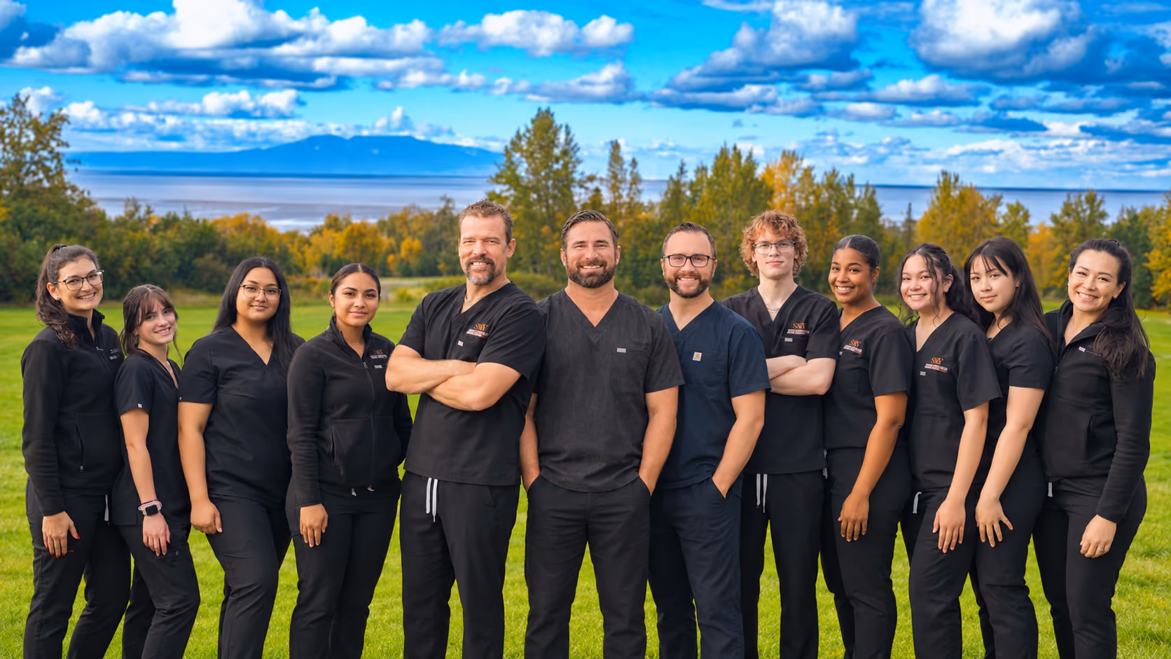 Muldoon Dental Arts team of dentists and staff standing outdoors in Anchorage, Alaska with mountains and trees in the background.